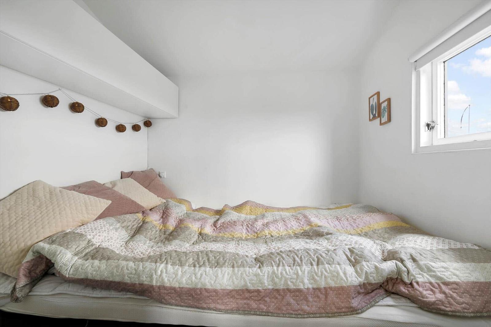Schlafzimmer mit Bett, Decke und Fenster. An der Wand hängt eine Lichterkette.