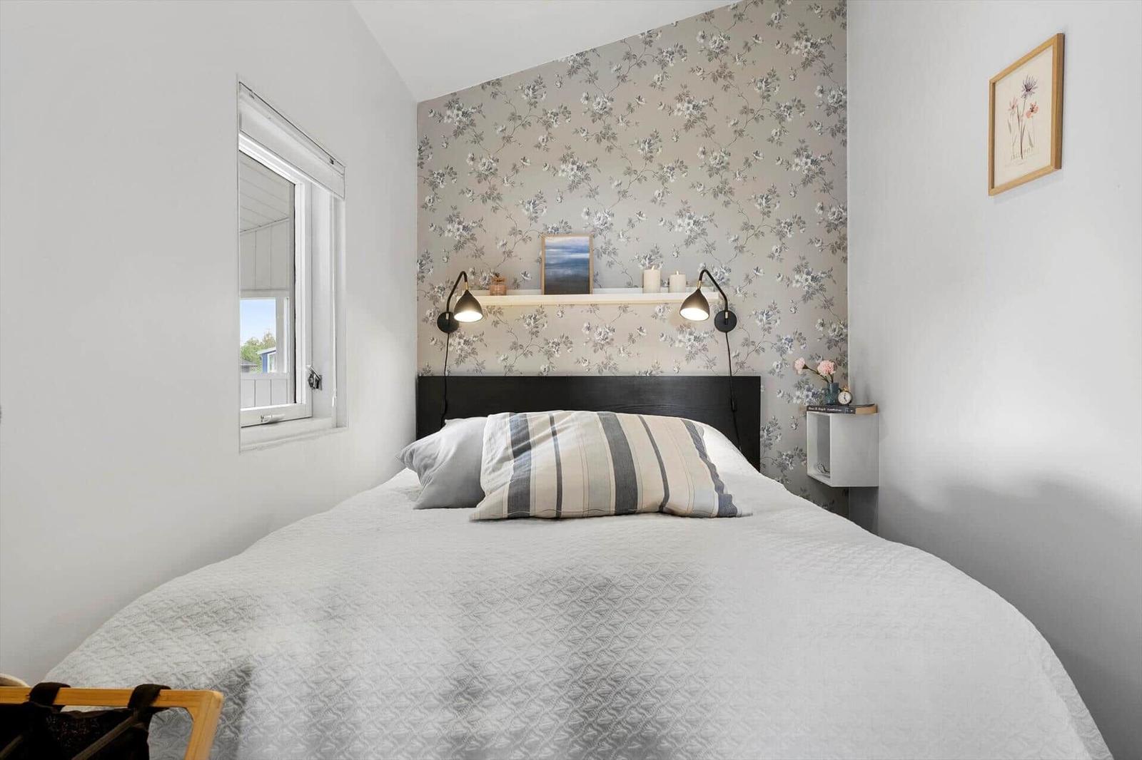 Schlafzimmer mit Bett, Blumenwand, Nachttisch und Fenster.