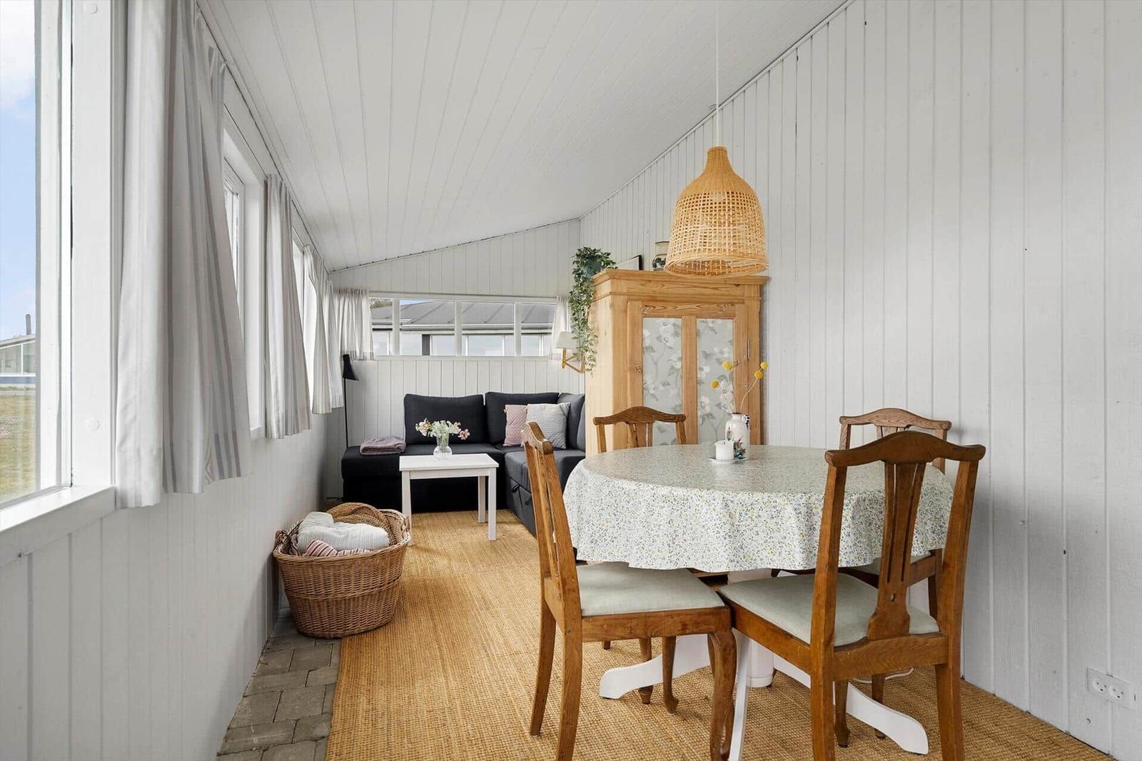 Essbereich mit runden Tisch und Holzstühlen. Im Hintergrund befindet sich ein Sofa und ein Schrank.