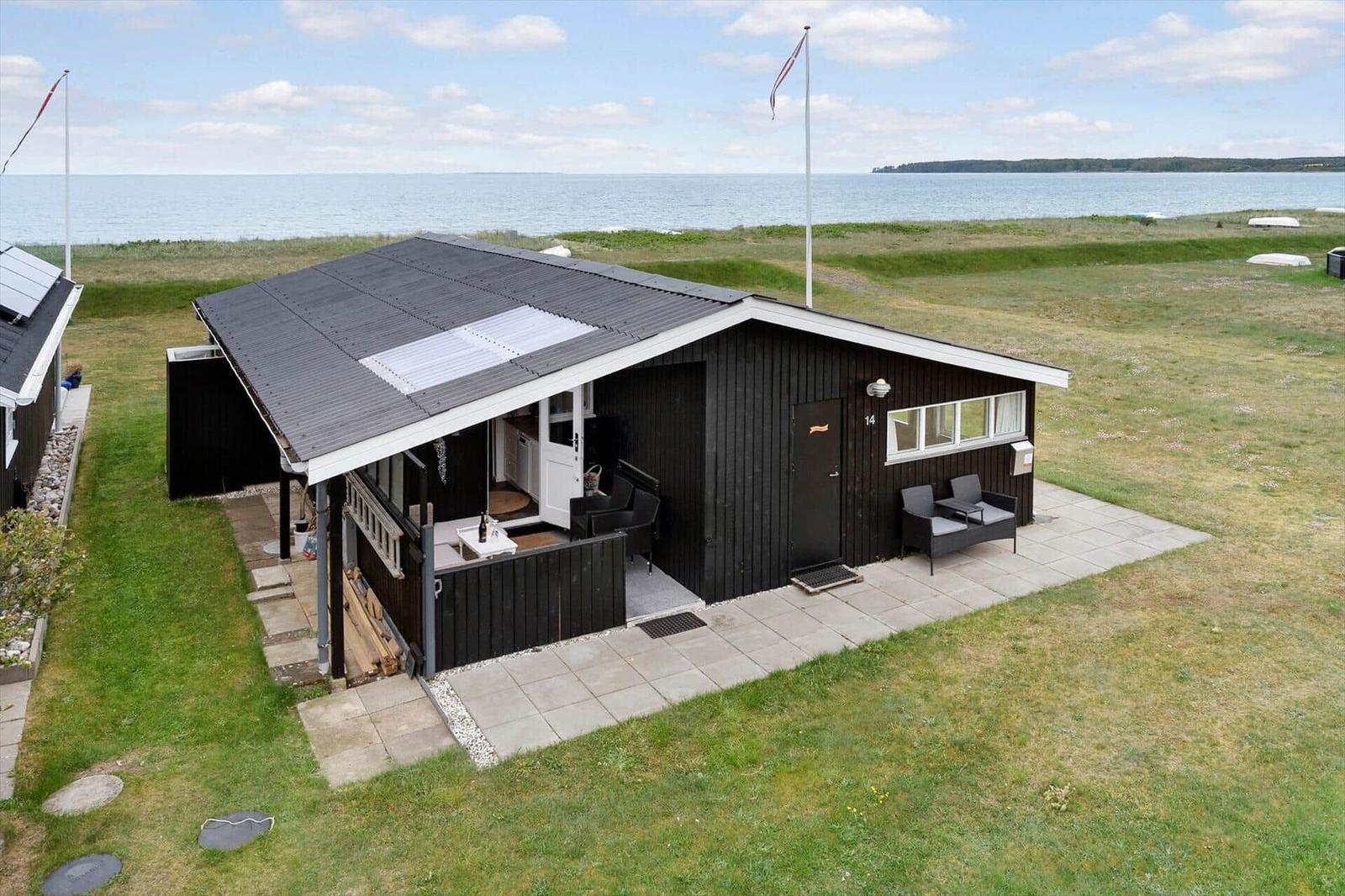 Ein schwarzes Strandhaus mit Terrasse, Garten und Meerblick. Flagge weht im Wind.