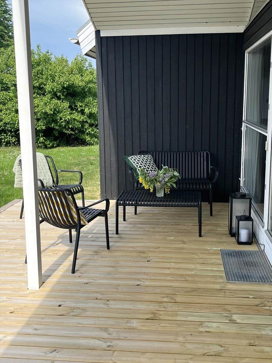 Terrasse mit Sitzgelegenheiten und Blumenarrangement vor schwarzem Holzhaus