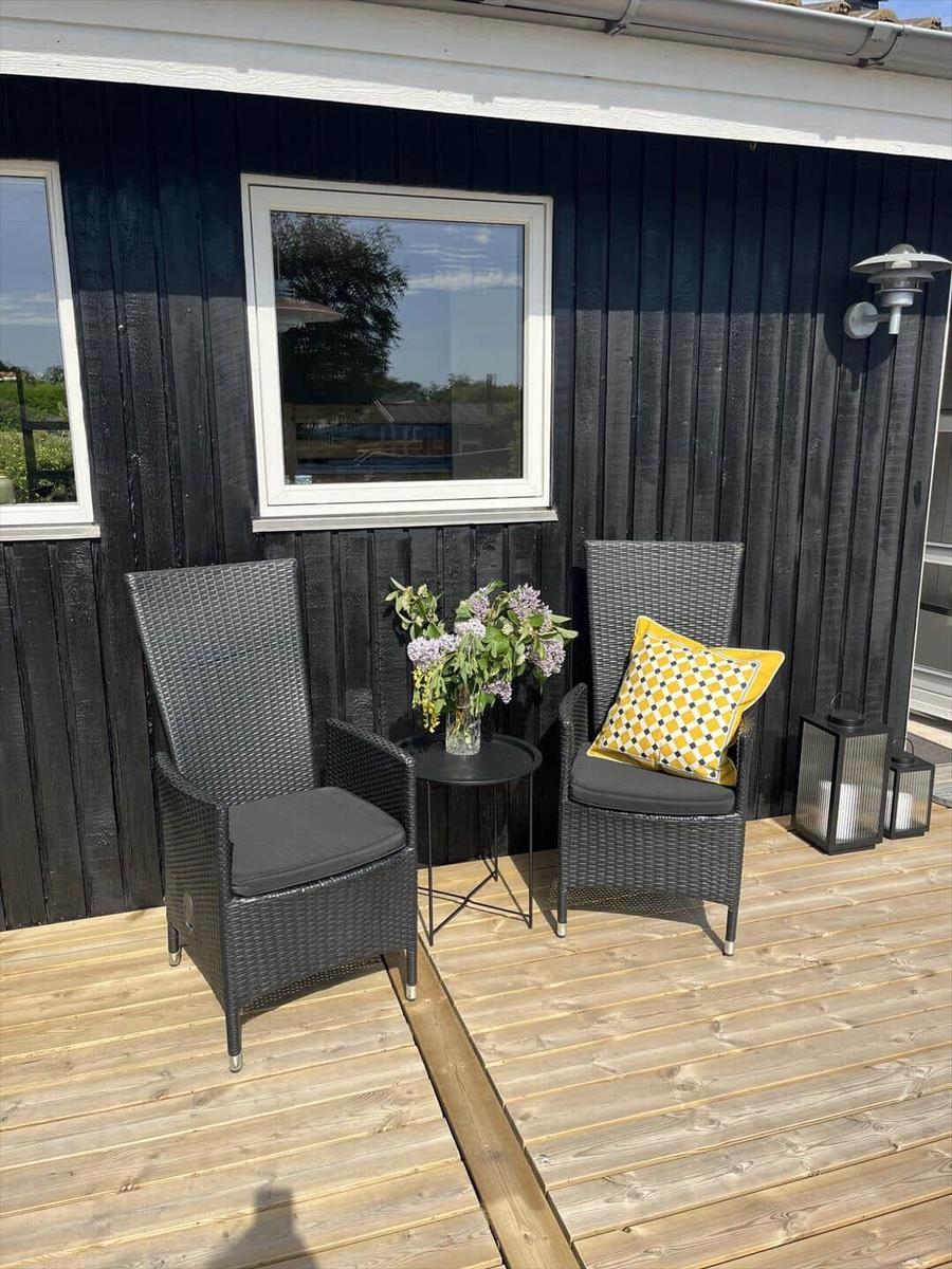 Terrasse mit zwei Stühlen, Tisch und Blumen vor schwarzem Holzhaus