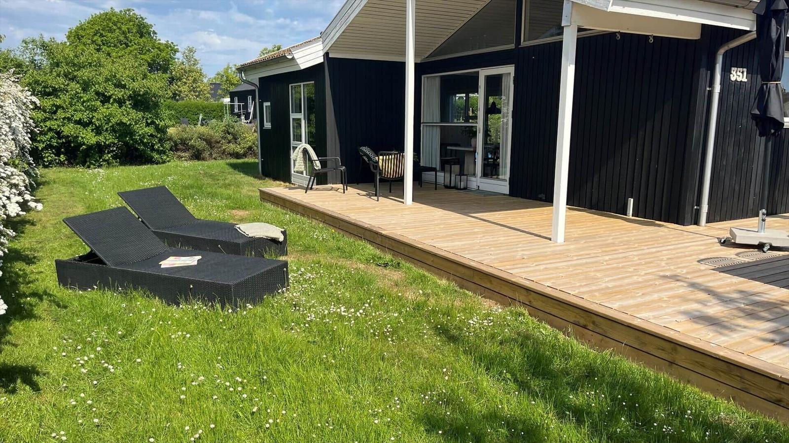 Haus mit Holzterrasse, Liegestühlen und grünem Rasen. Hausnummer 351.