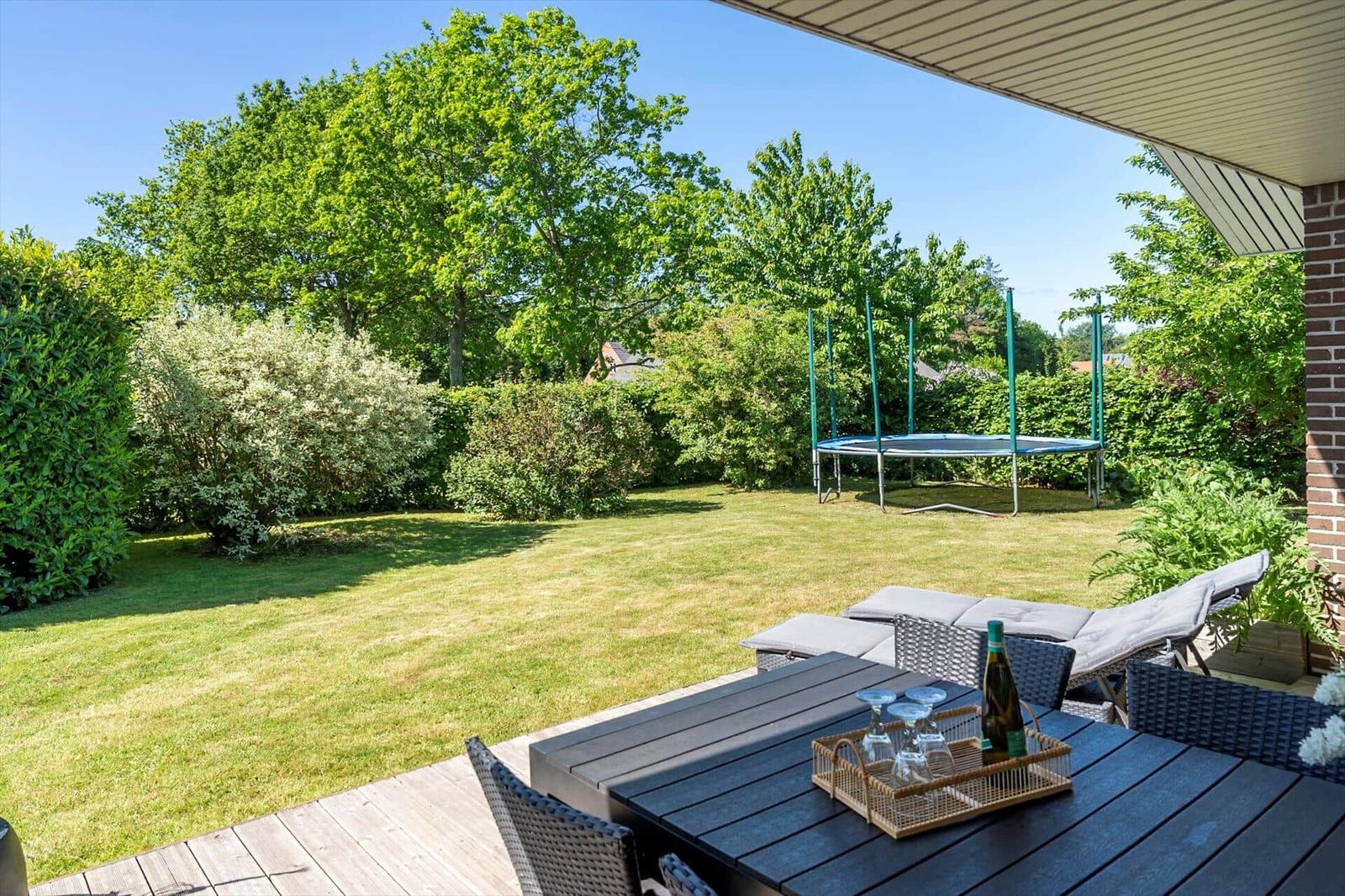 Terrasse mit Tisch, Stühlen und Trampolin im Garten.