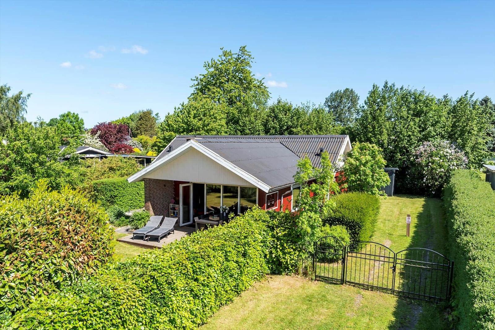 Rotes Haus mit Terrasse und Garten. Umgeben von Bäumen und Hecken.