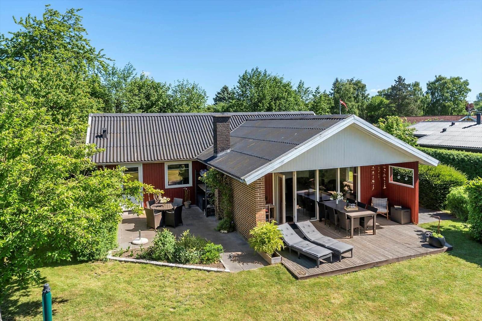 Roter Holzhaus mit Terrasse, Garten und Grillplatz. Modernes Design mit Holz- und Steinverkleidung.