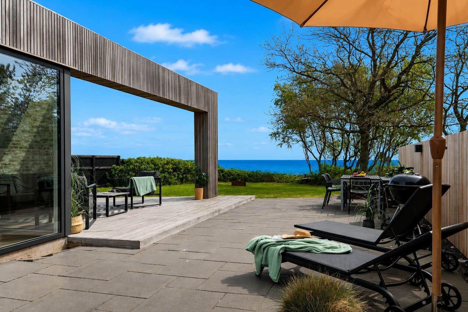 Terrasse mit Liegestühlen, Grill und Blick auf das Meer.