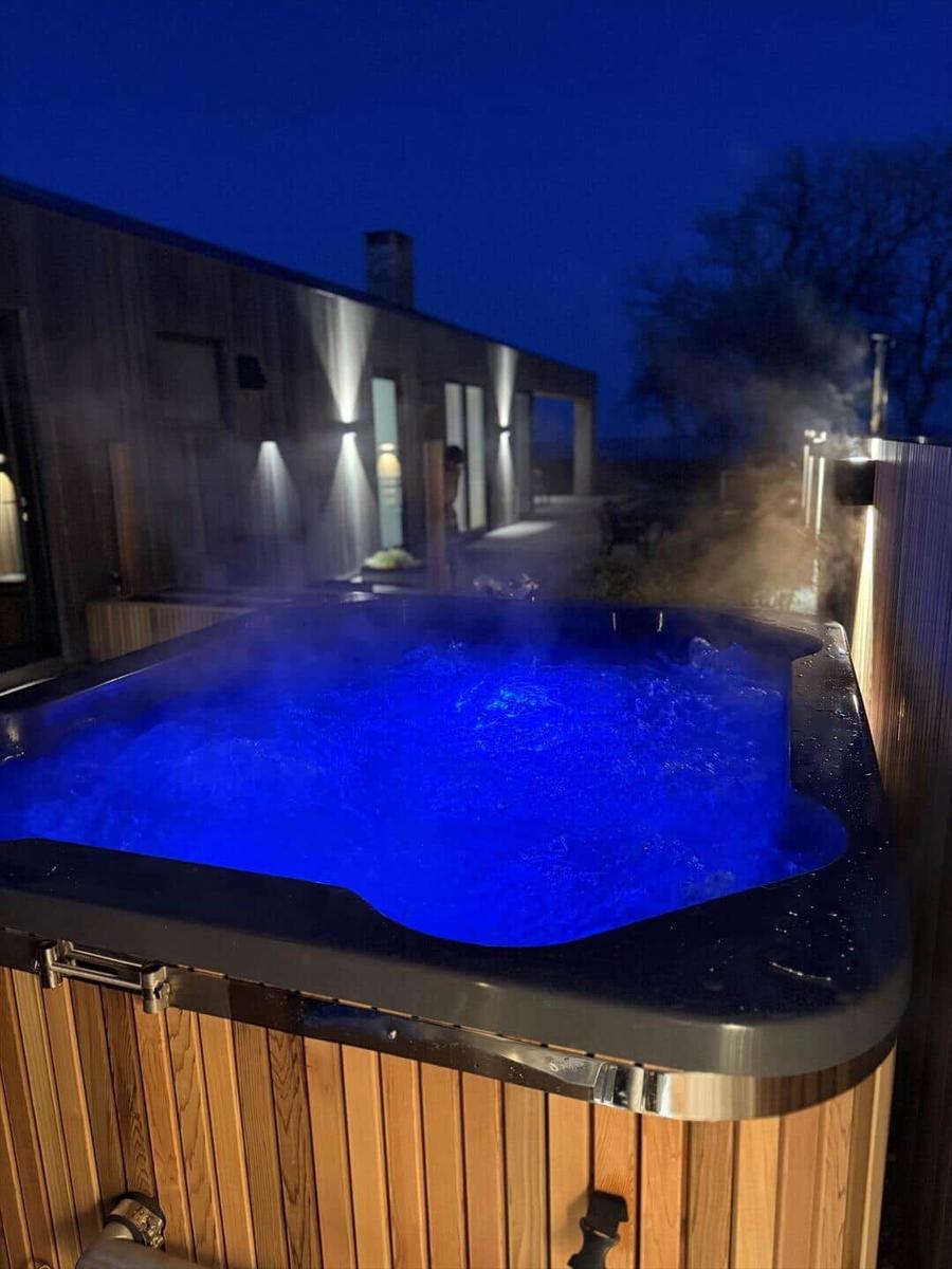 Ein beleuchteter Whirlpool mit Dampf bei Nacht vor einem modernen Haus.