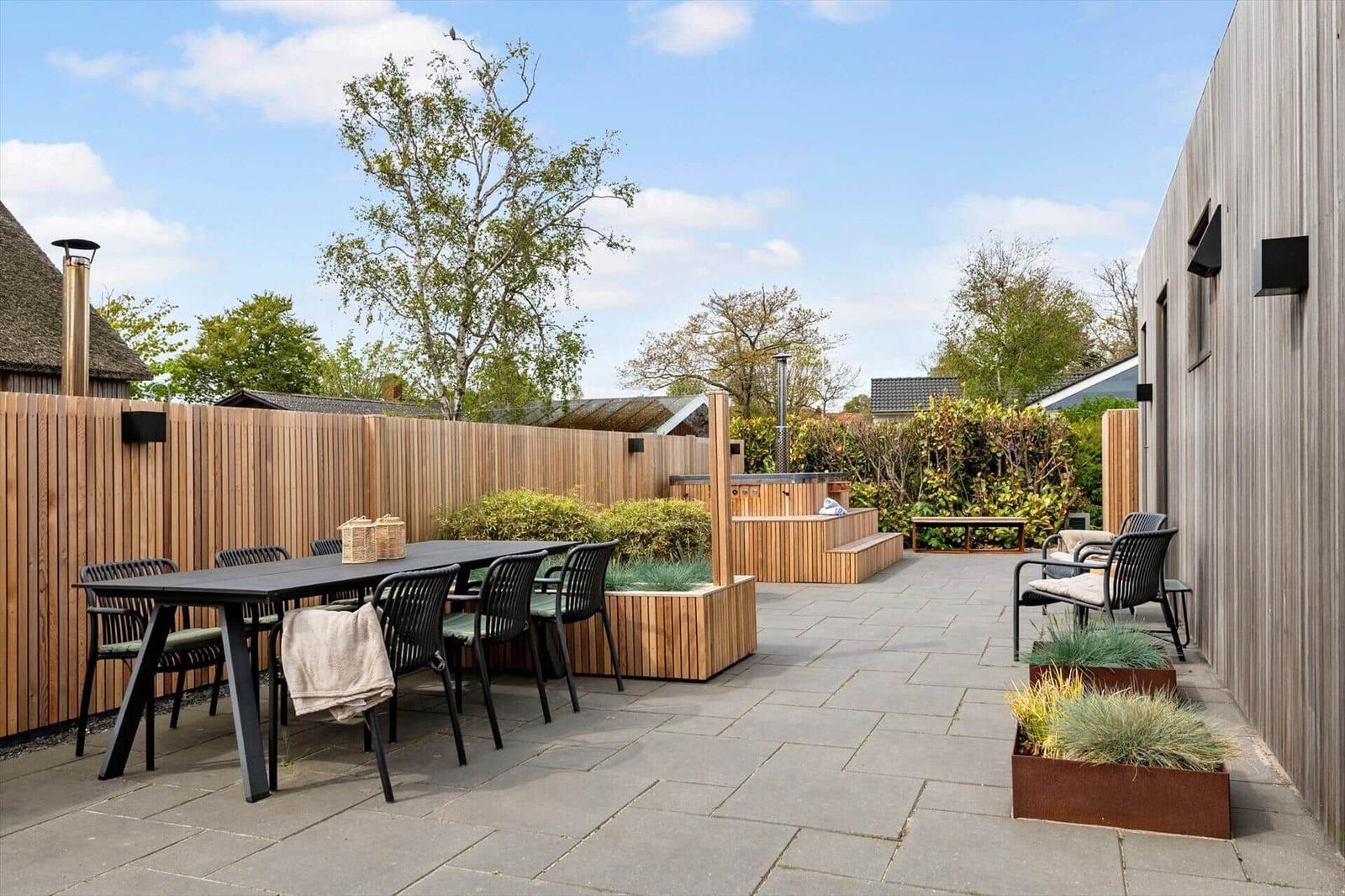 Terrasse mit Tisch, Stühlen und Whirlpool. Holzgeländer und Pflanzen.