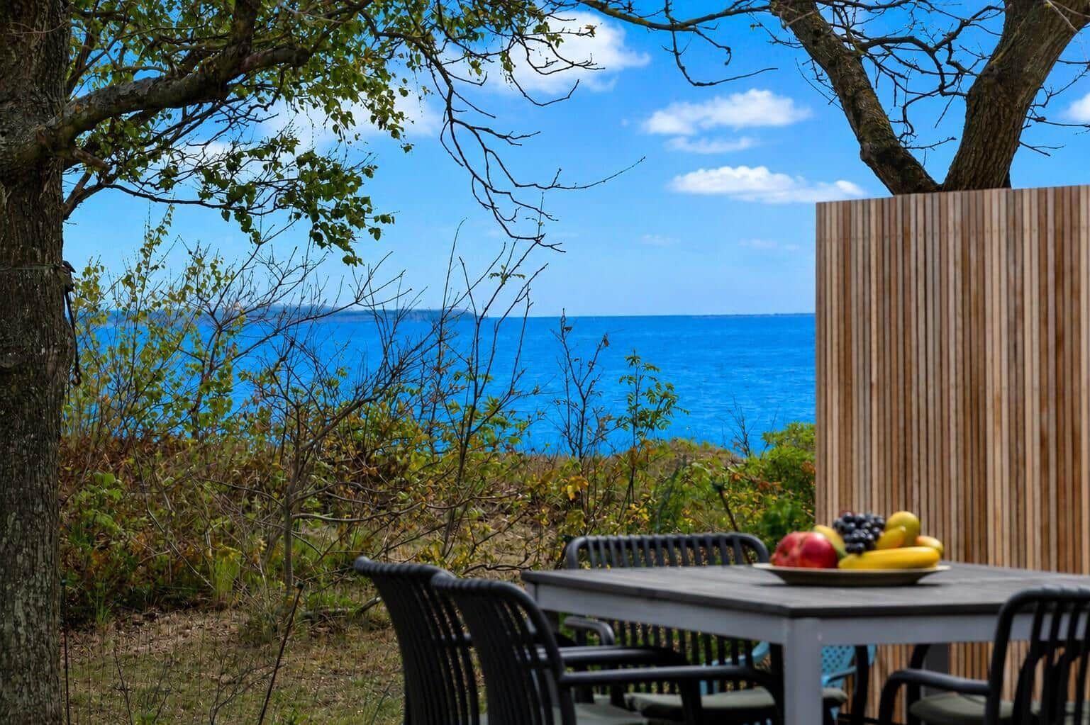 Terrasse mit Tisch und Stühlen, Blick auf das blaue Meer unter Bäumen.