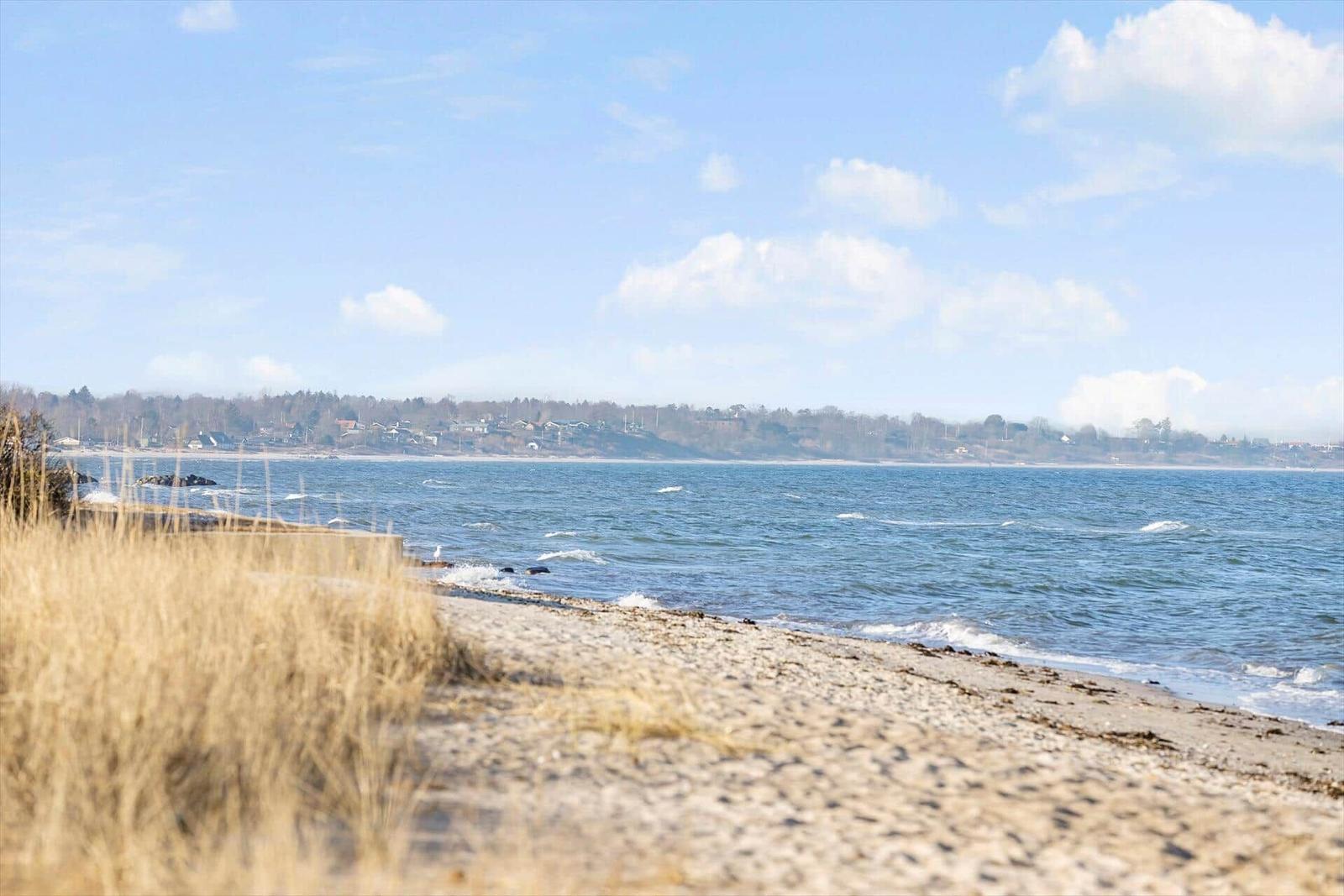 Strand mit Sand und Gras, Meer und Himmel mit Wolken im Hintergrund.