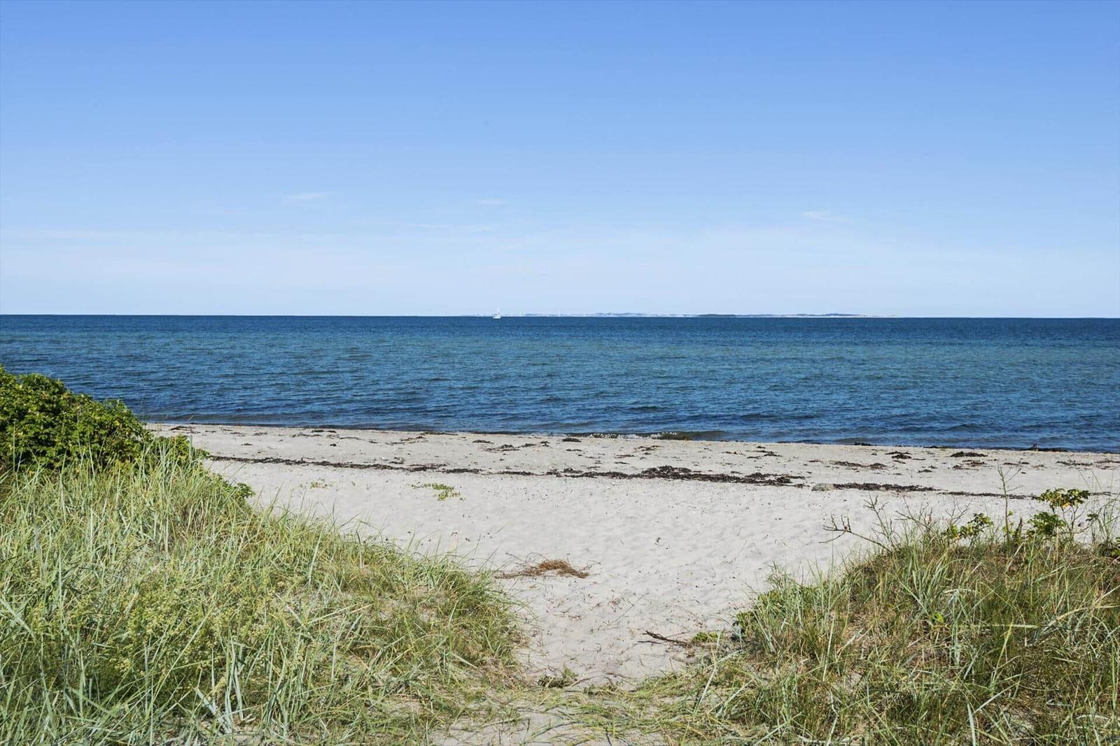 Strand mit Sand und Gras, Blick auf das Meer unter blauem Himmel.