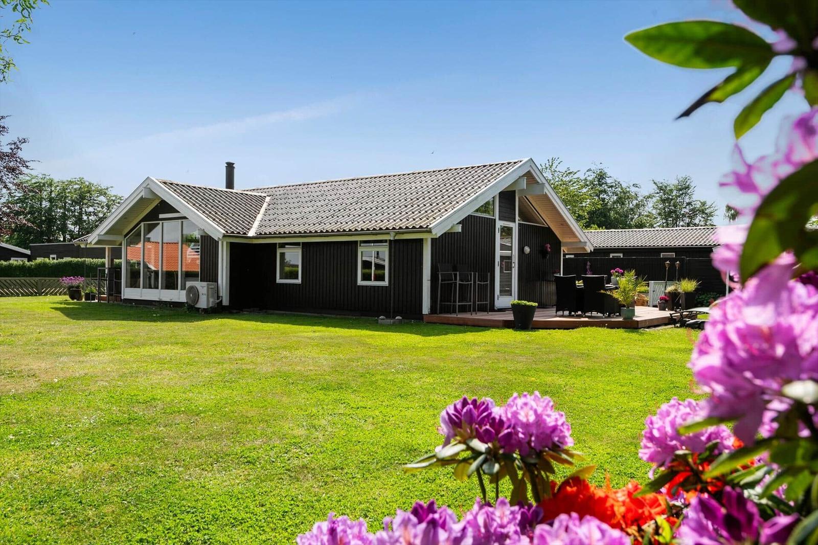 Haus mit Garten und Terrasse. Blumen im Vordergrund.
