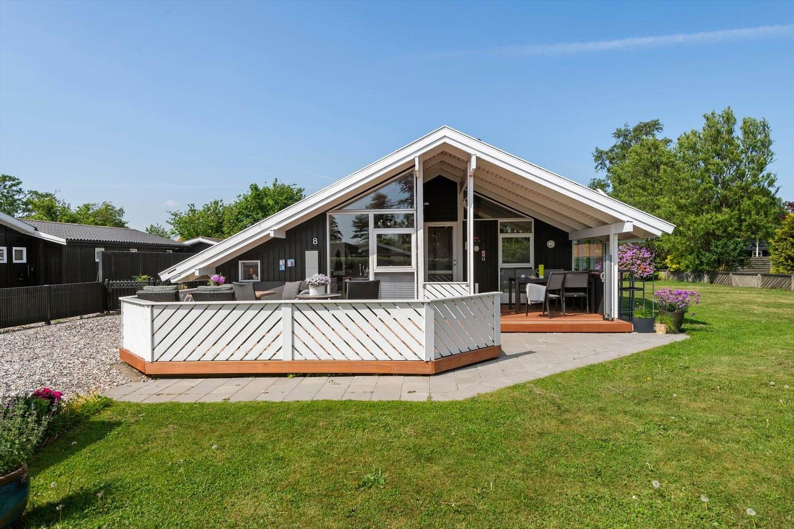 Moderne Ferienhaus mit Terrasse, Garten und Holzveranda. Schwarze Fassade und große Fenster.
