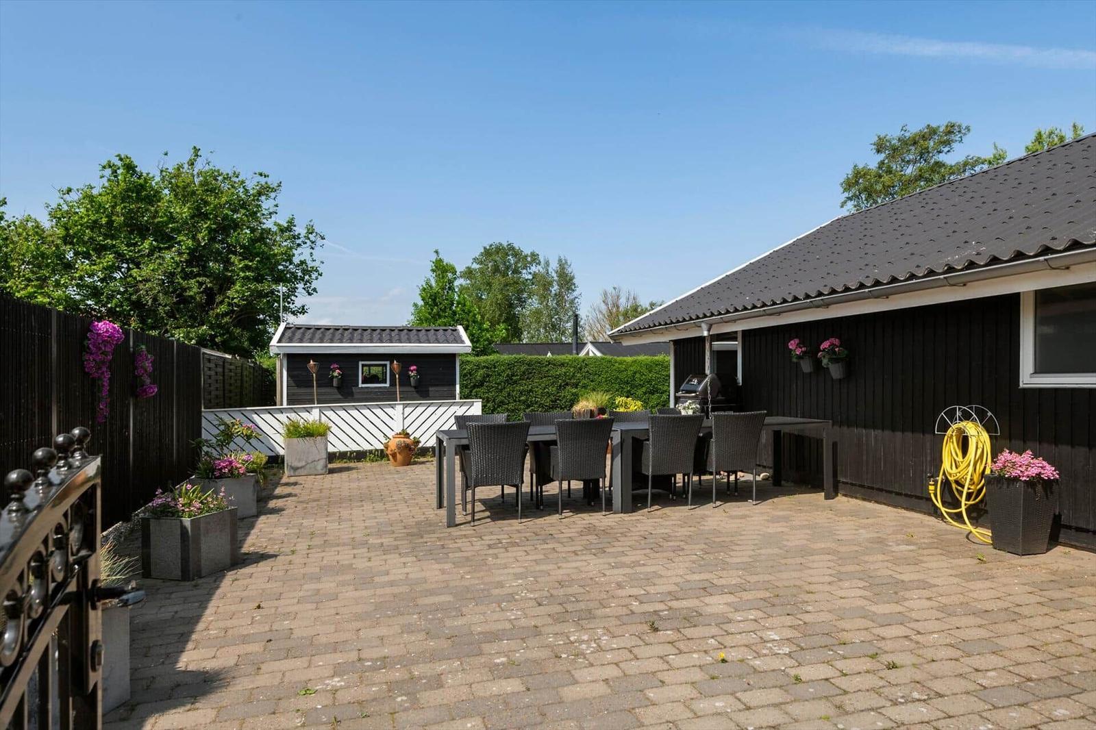 Terrasse mit Sitzgruppe, Grill und Pflanzen. Hinterhof mit kleinem Haus und Zaun.