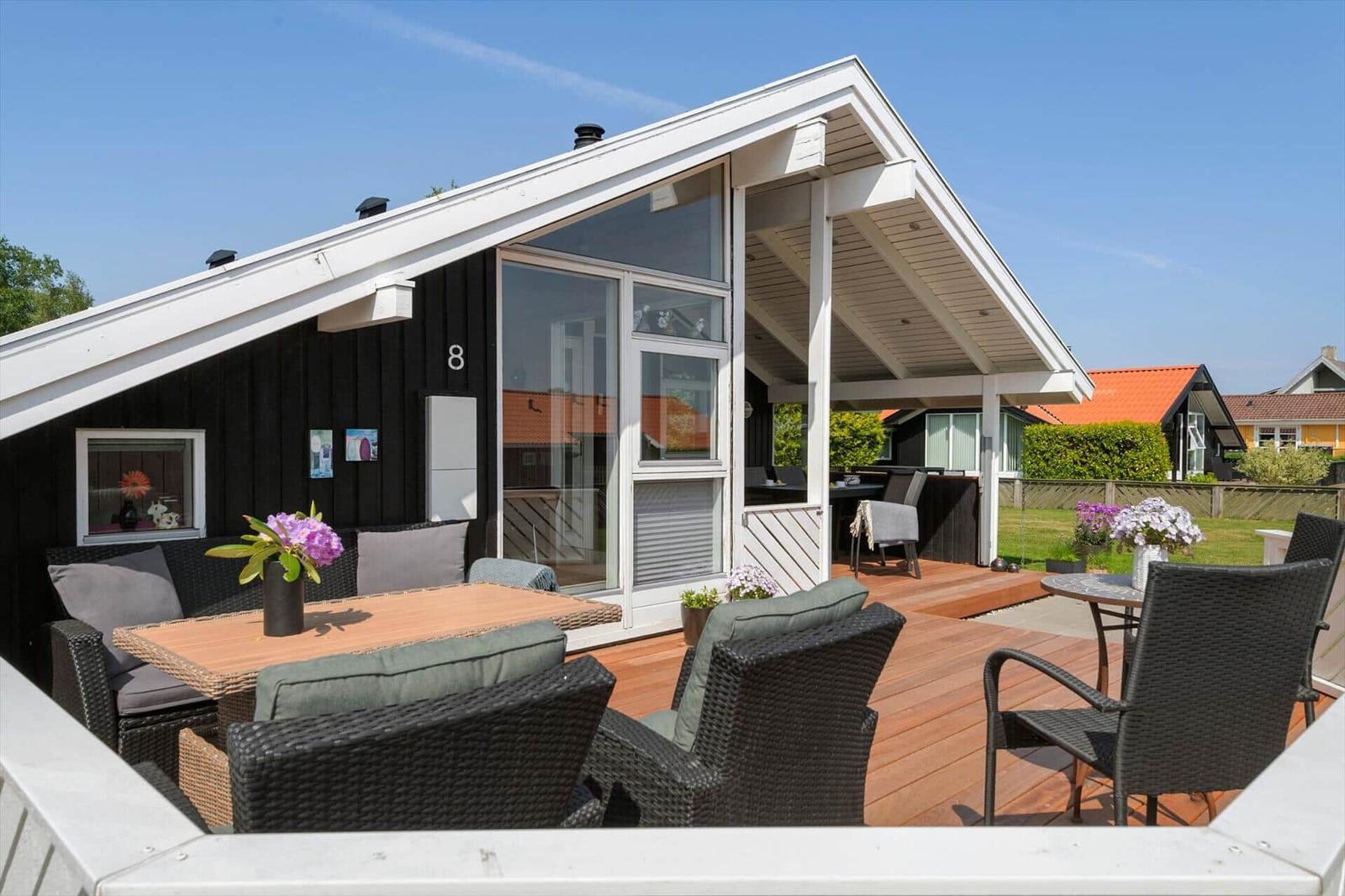 Terrasse mit Sitzgruppe und Tisch vor einem Haus mit schwarzem Holz und weißen Rahmen.