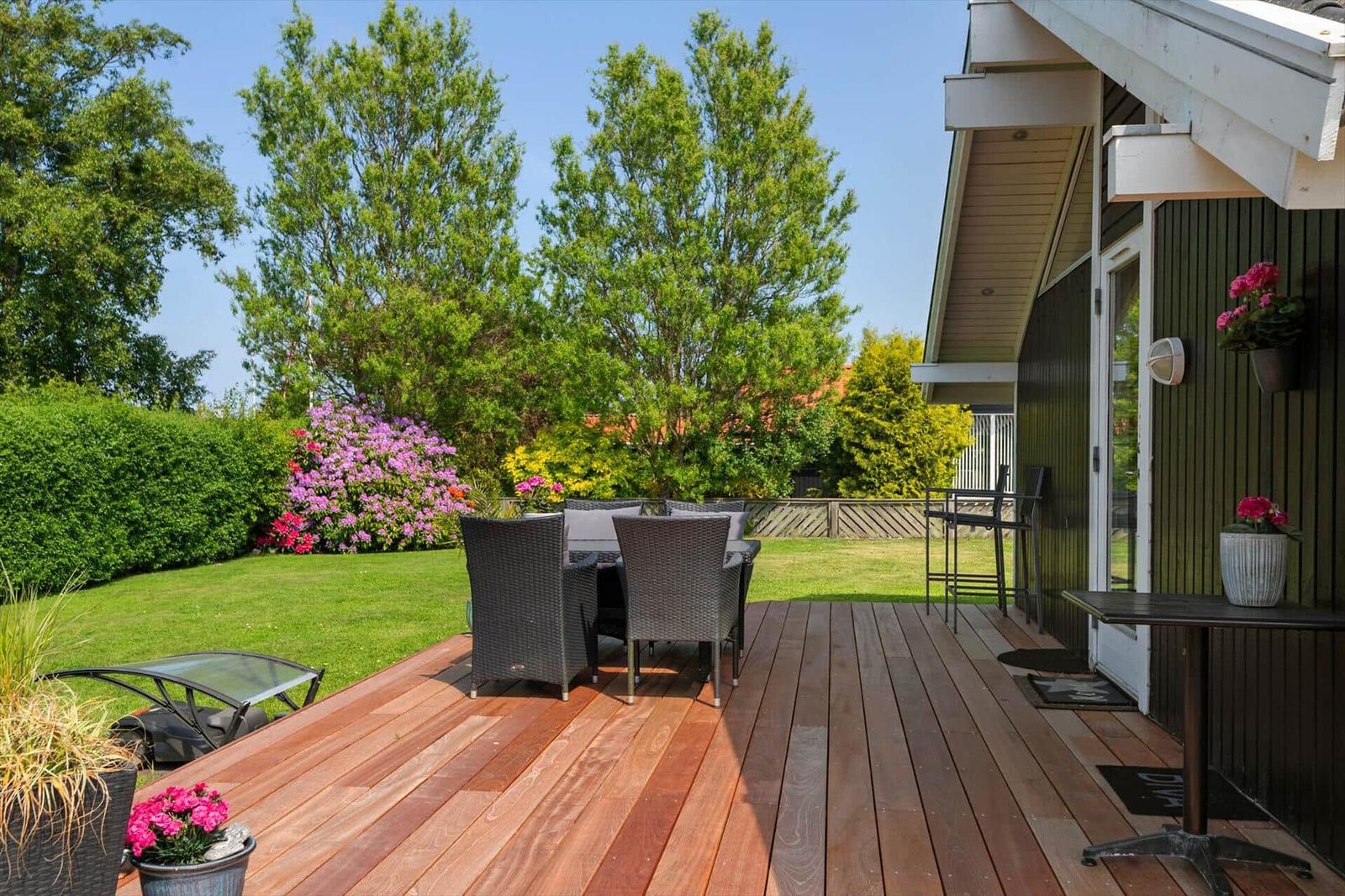 Terrasse mit Sitzgruppe, Blumen und Blick auf grünen Garten.