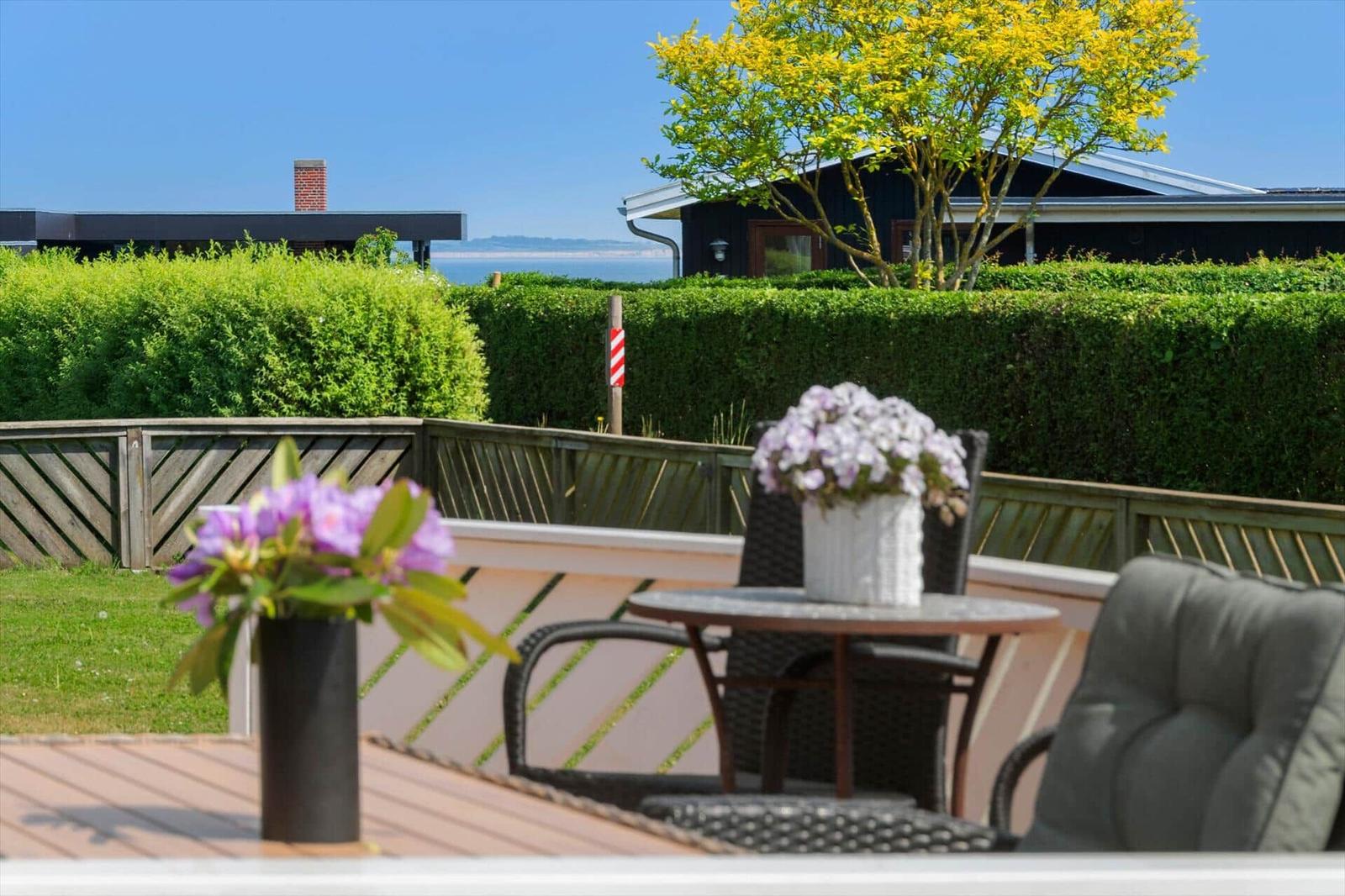 Terrasse mit Tisch, Stühlen und Blumen. Blick auf grüne Hecke und Meer.