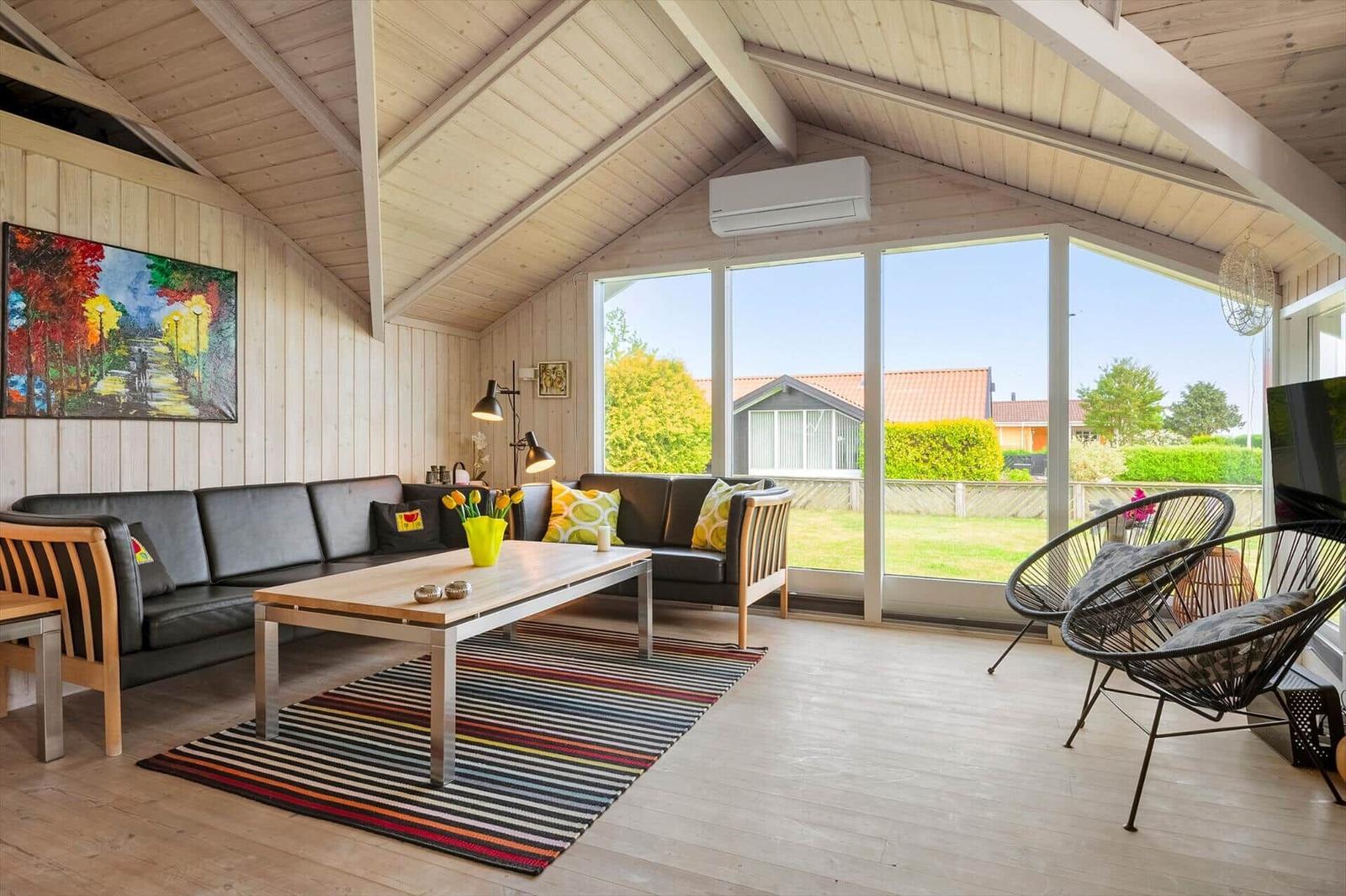 Wohnzimmer mit Sofa, Tisch und Sessel. Große Fenster und Holzwände.