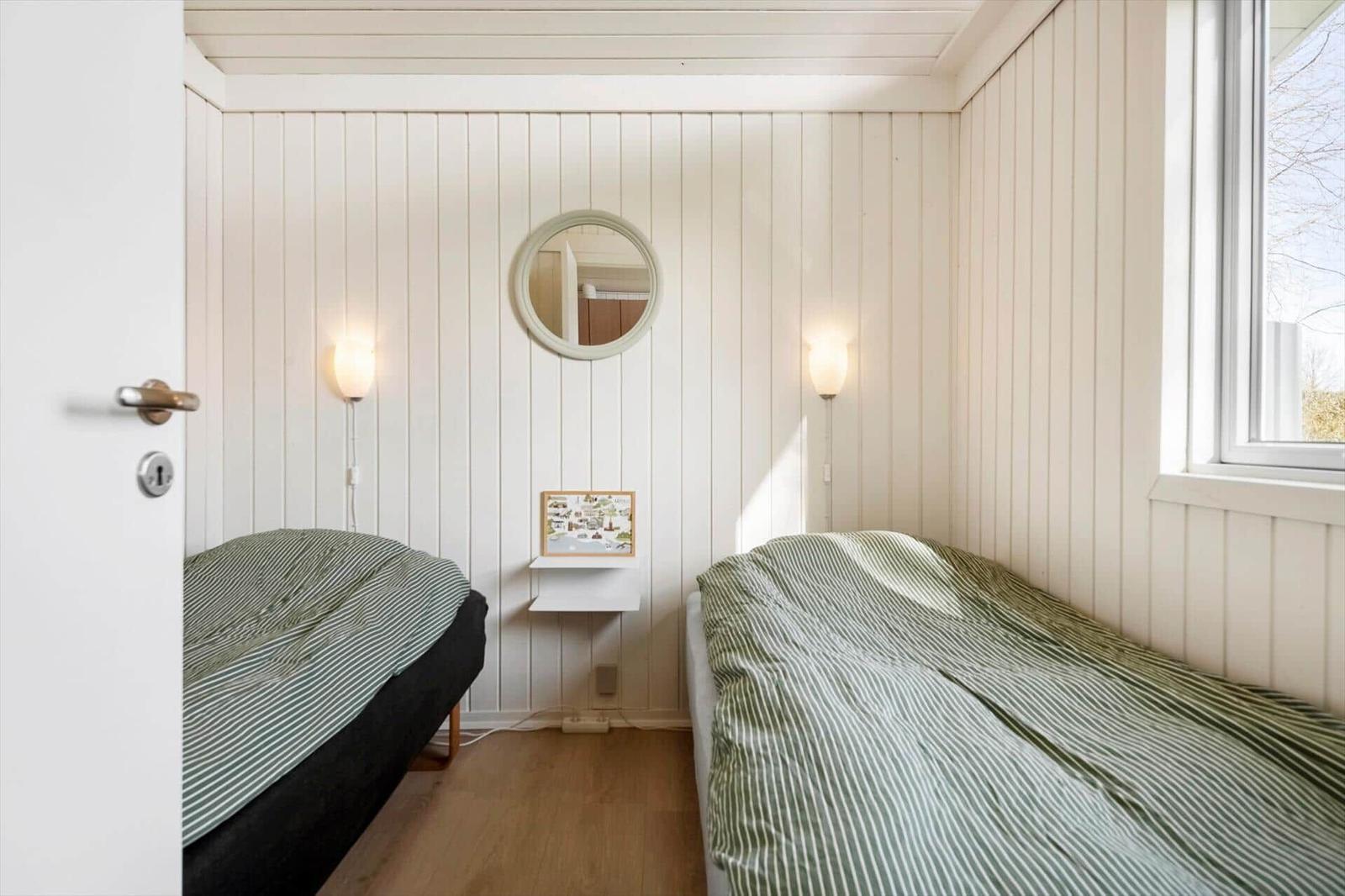 Two beds with striped bed covers, white wood walls, round mirrors and wall lamps.