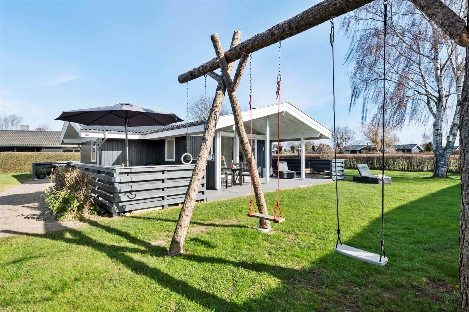 House with terrace, swings, and lawn. Garden area with lounge chair and umbrella.