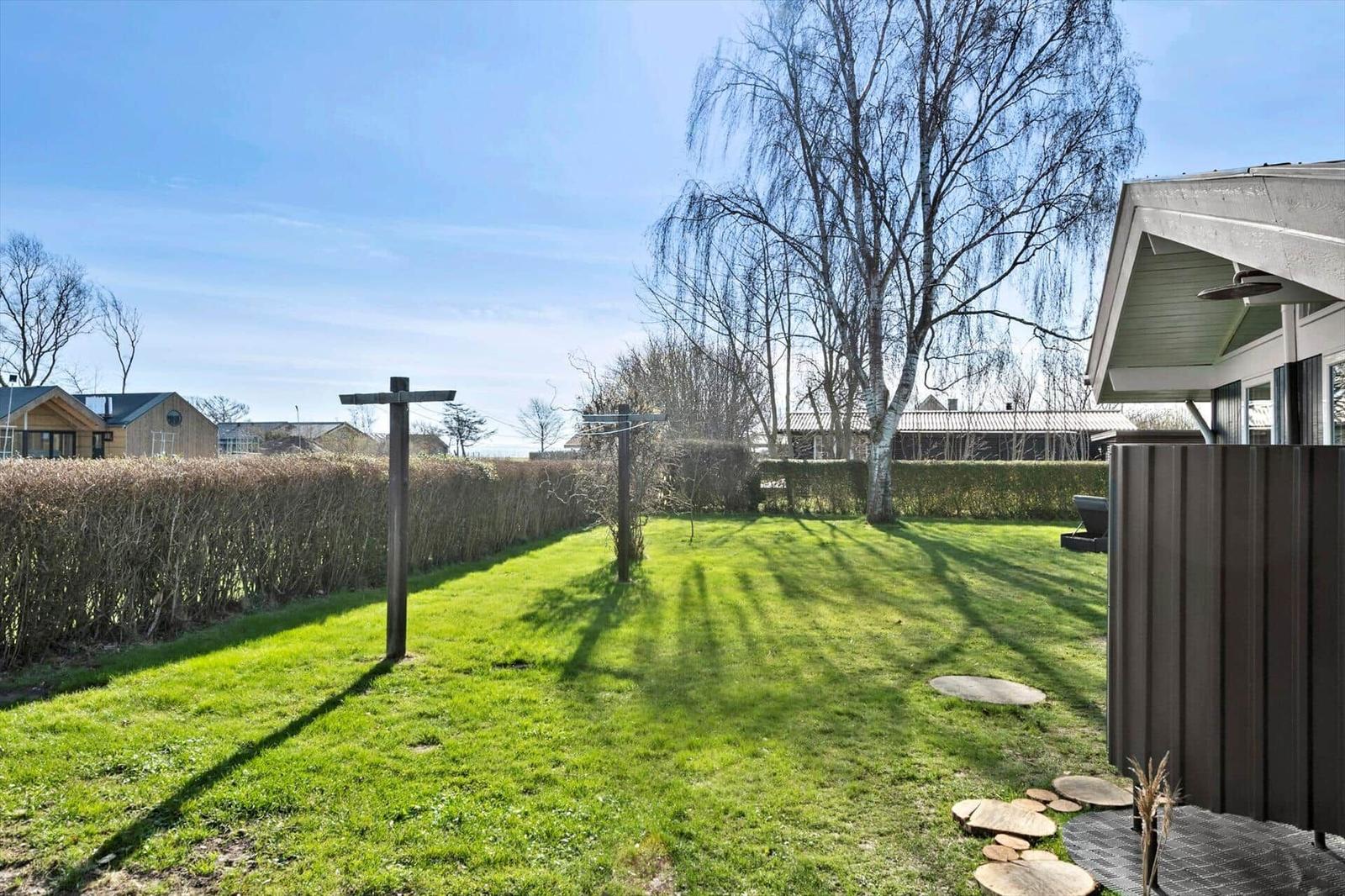 Green lawn area with trees and wooden posts. Buildings and hedges are visible in the background.