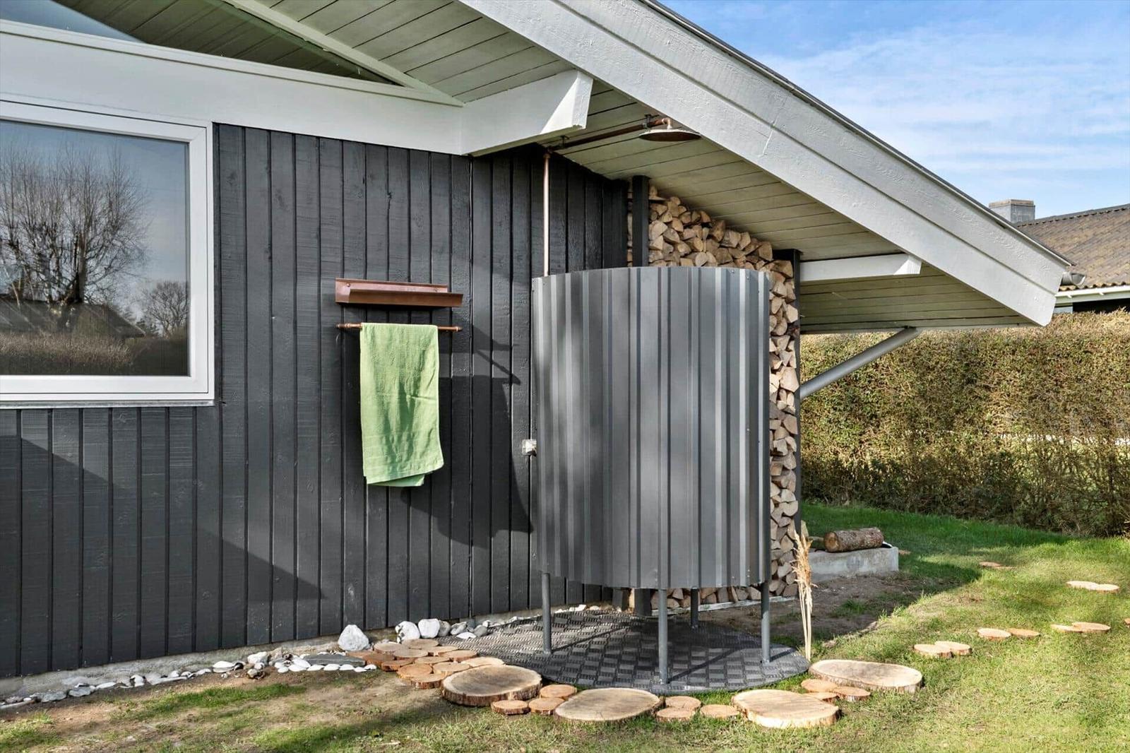 Outdoor shower with woodpile and green towel on house wall