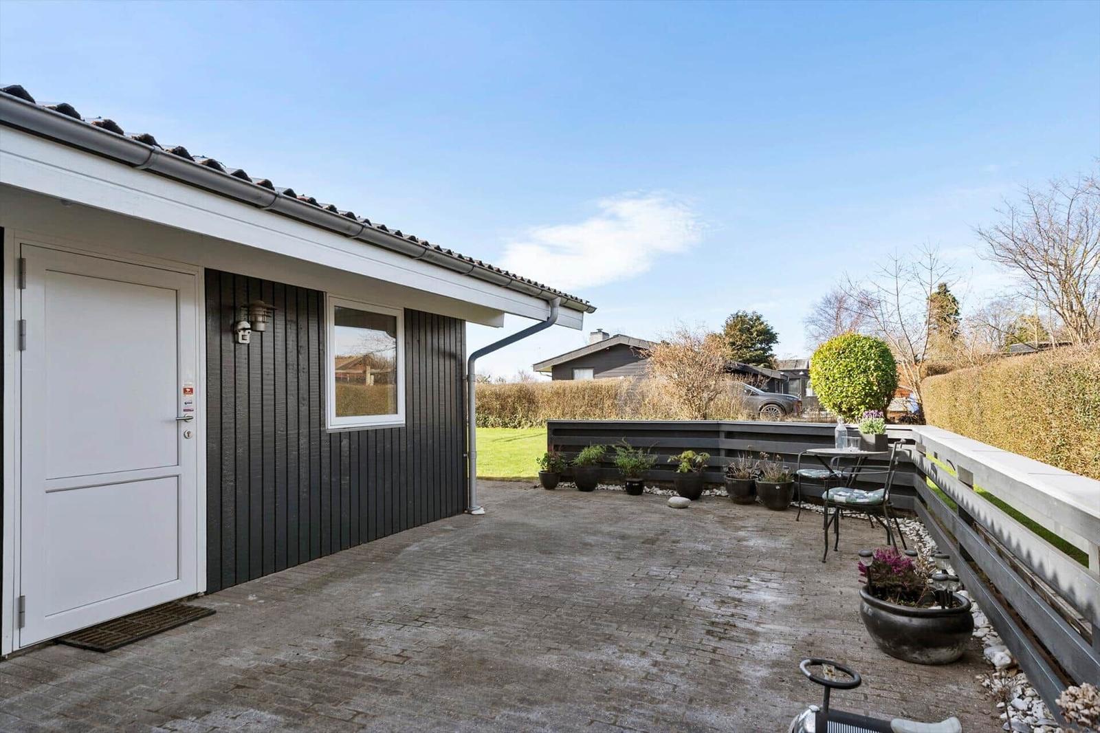 House with terrace, plants, and garden. White door and dark facade.