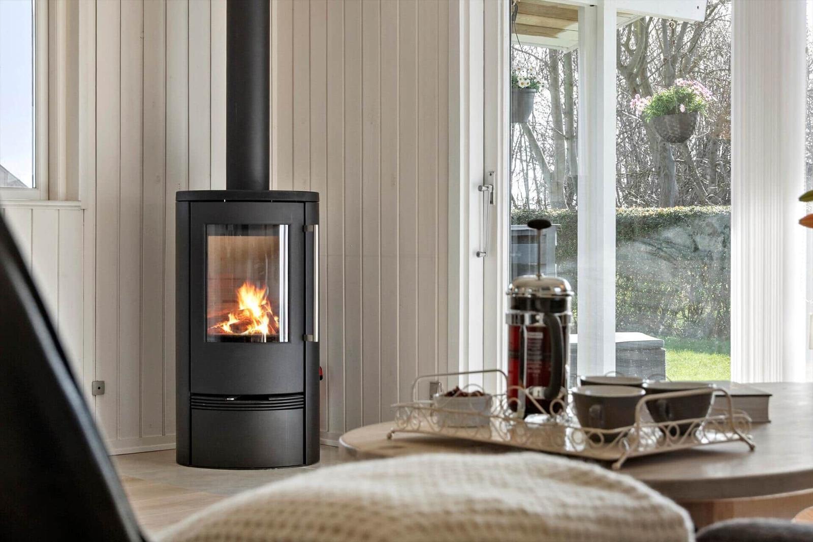A wood stove is in the living room with a view of a garden.