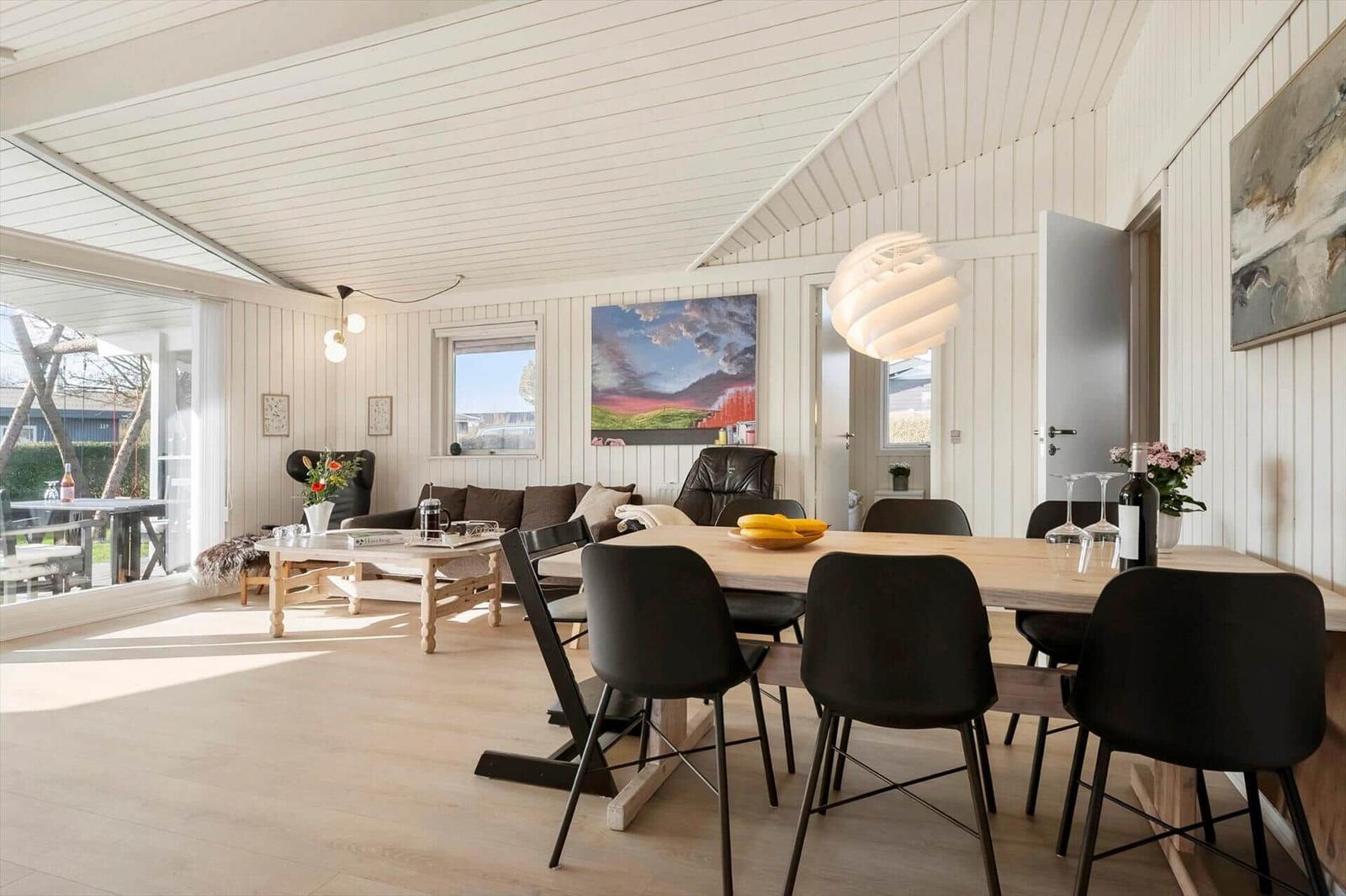 Dining area with wooden table and black chairs. Living area with sofa and window.