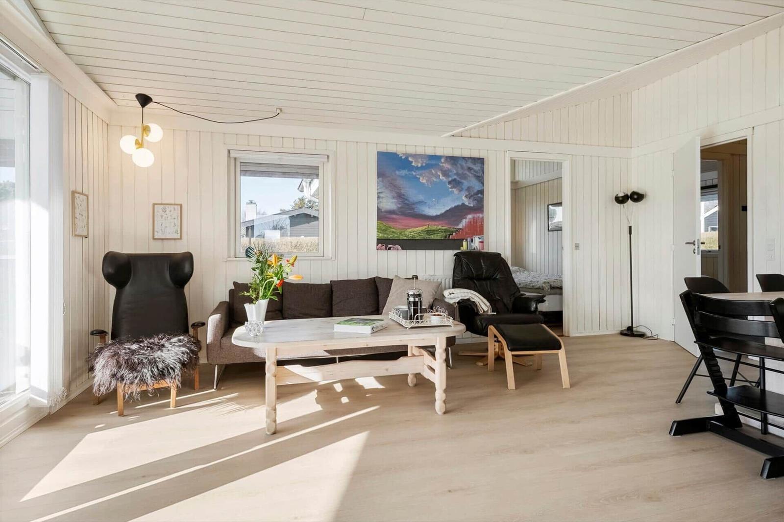 Living room with sofa, table, and chairs. Wall painting and window visible.