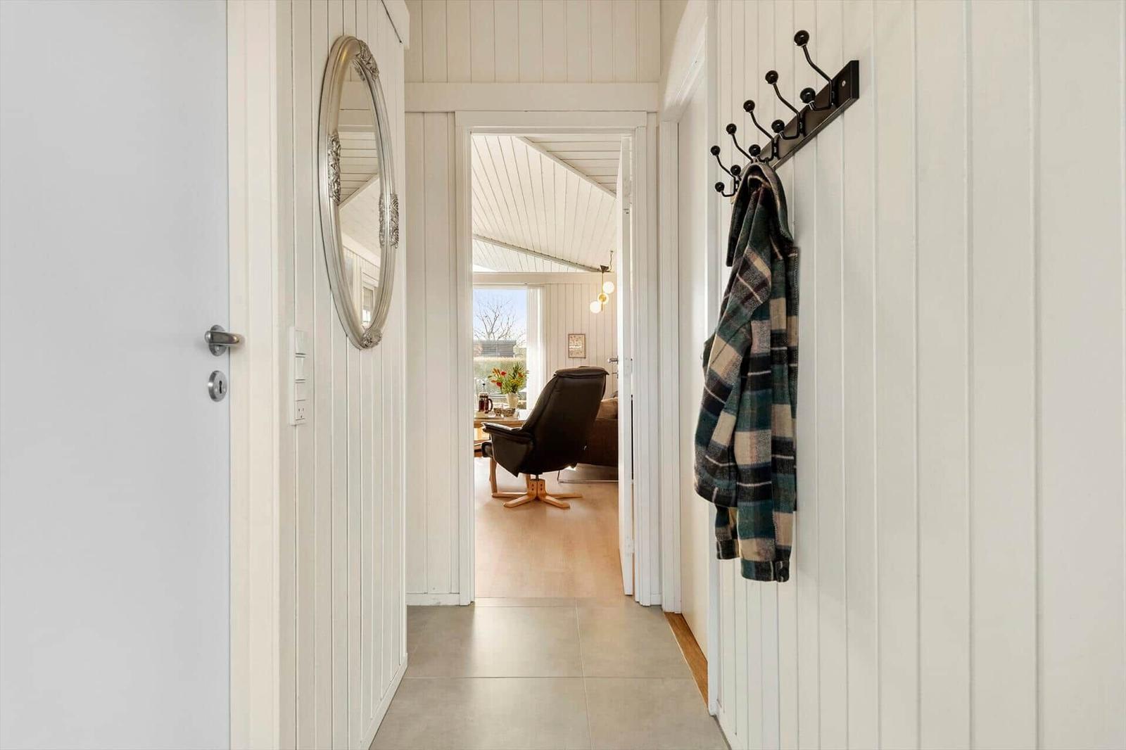 Hallway with mirror, coat rack, and view into living room with armchair.