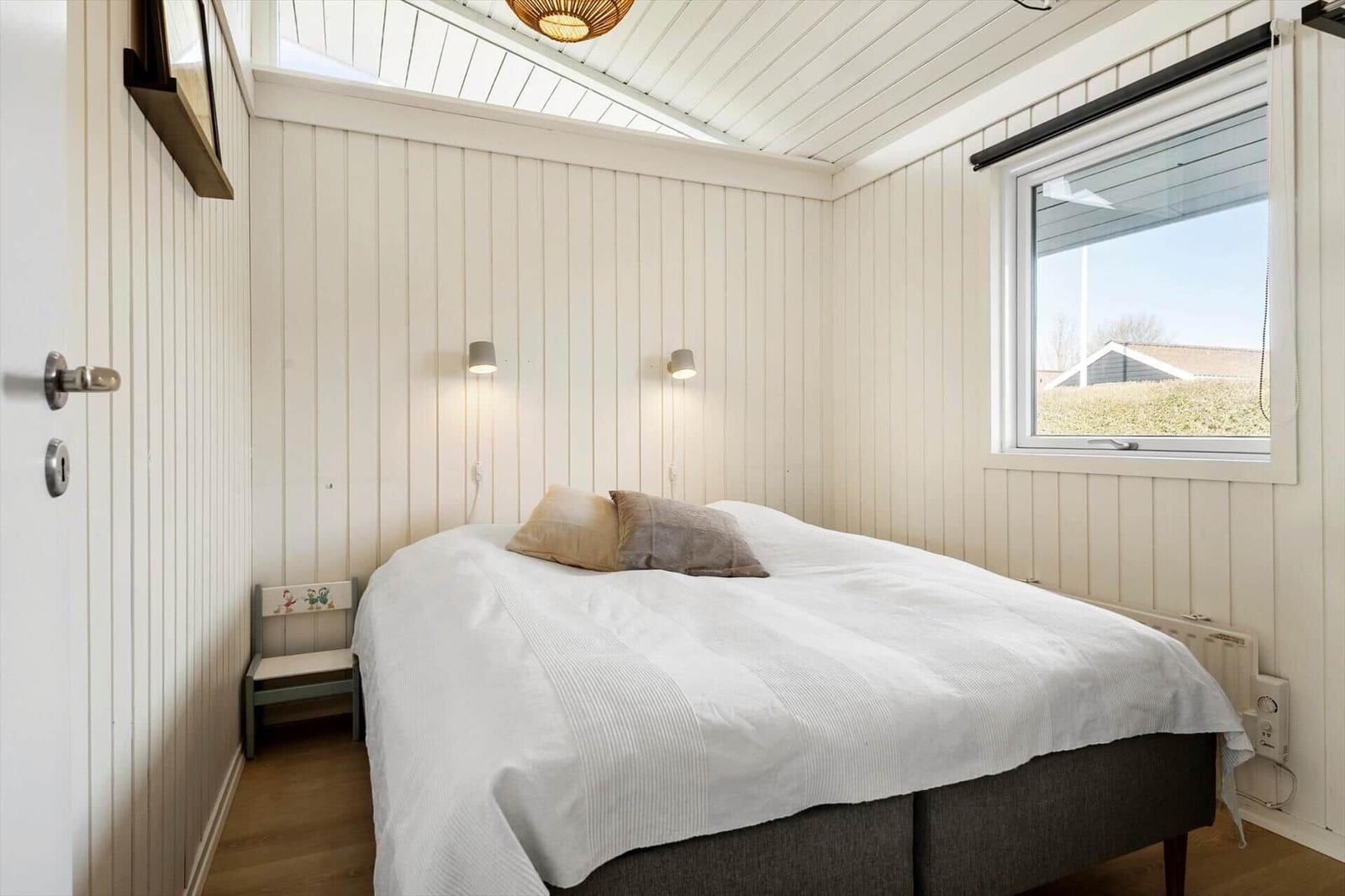 Bedroom with double bed, window, and ceiling light. Panel walls and wooden floor.