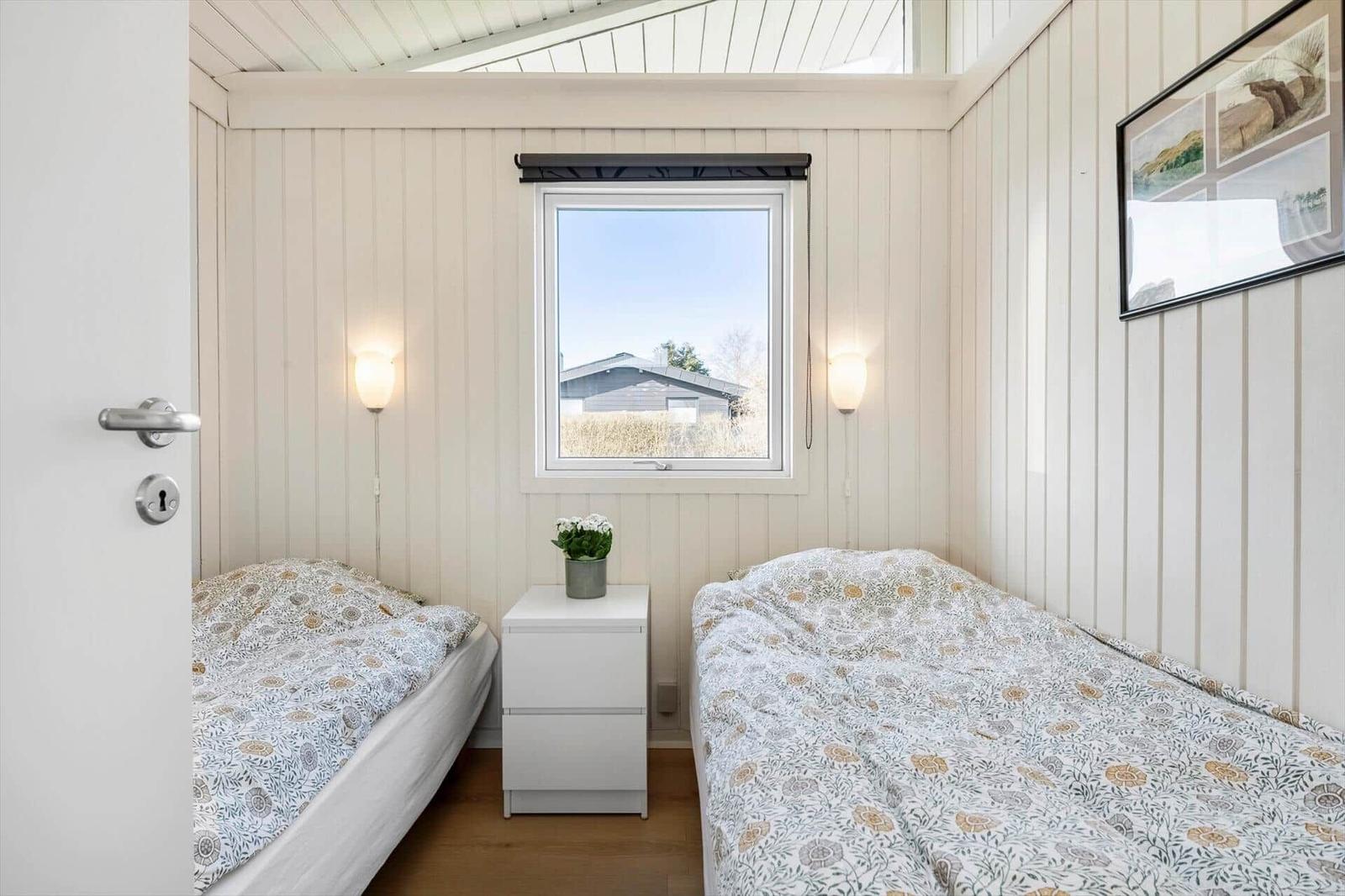 Two beds with patterned bedding, window with view outside, and nightstand.