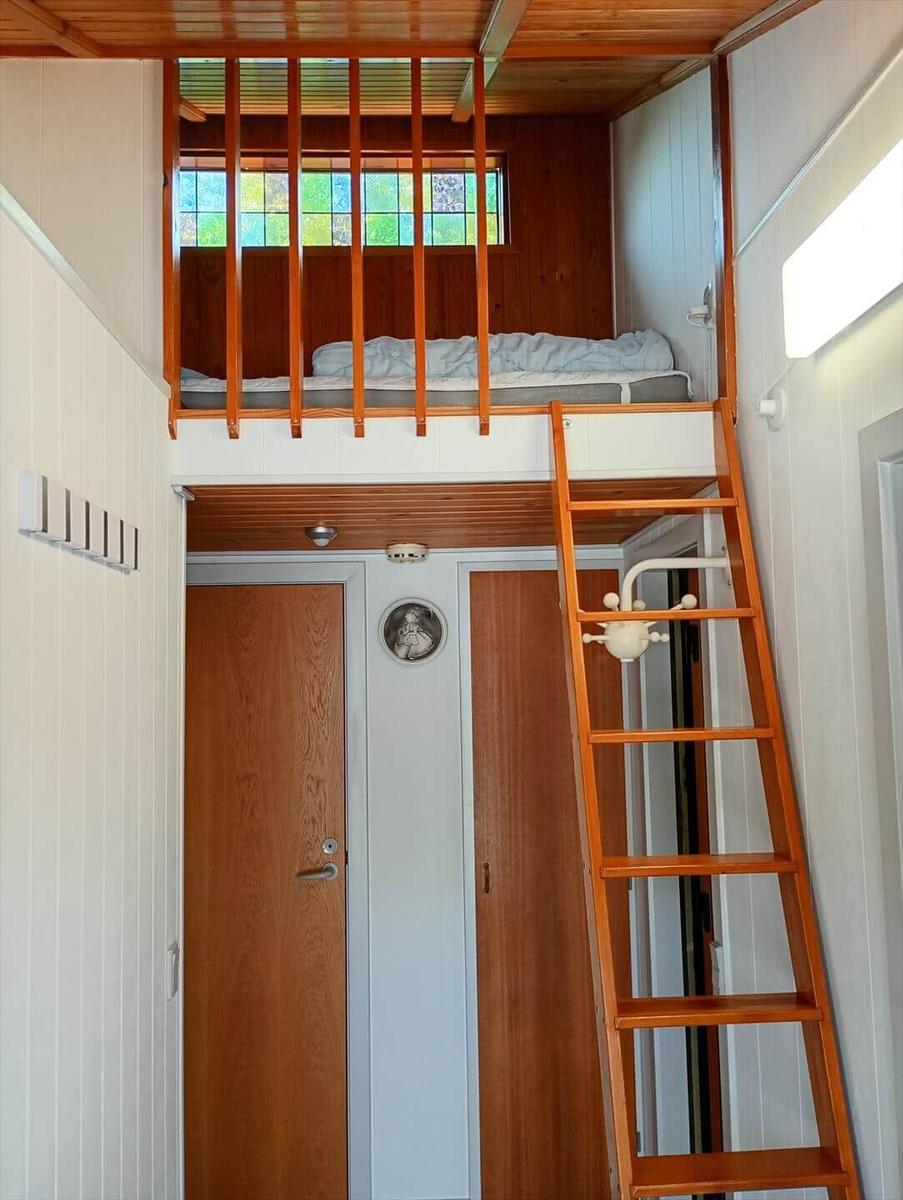Oben befindet sich ein Schlafbereich mit Bett und Fenster. Eine Leiter führt dorthin.