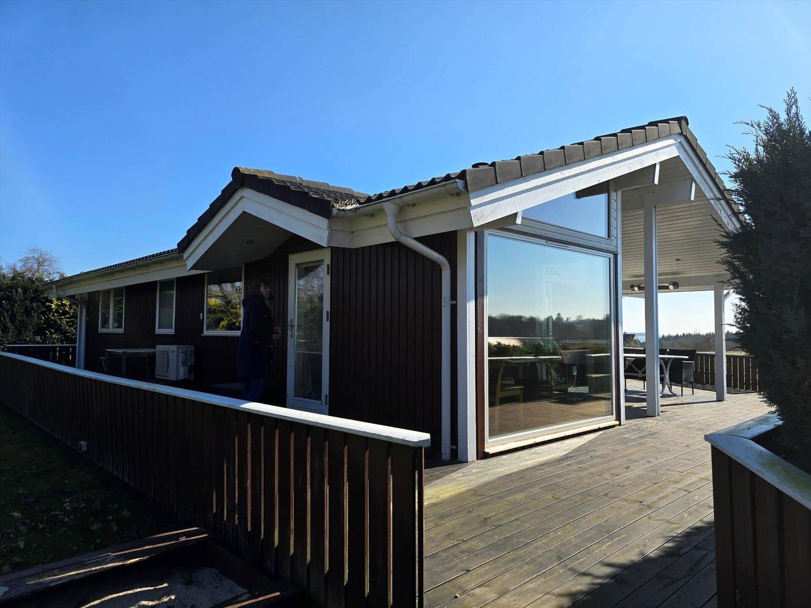 Moderne Villa mit Holzterrasse und großem Glasbereich. Personen sind im Außenbereich sichtbar.