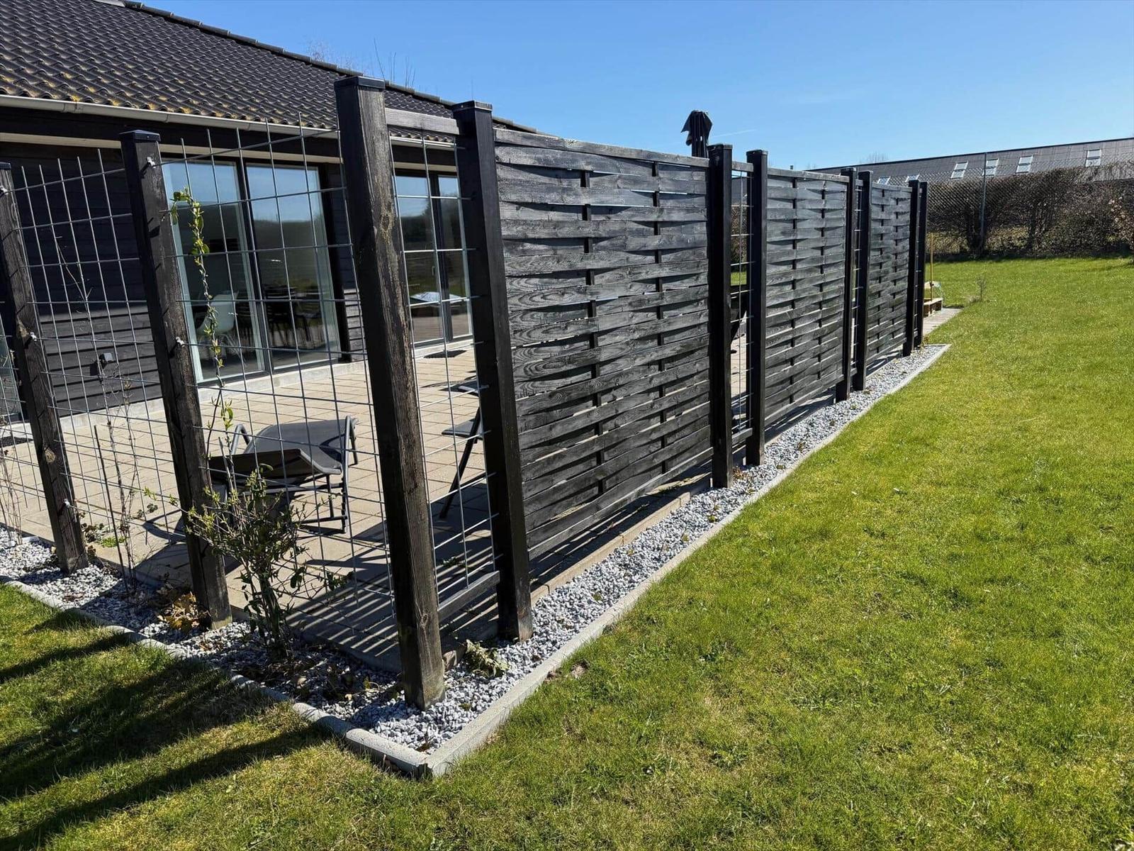 Hinterhof mit Holzgeländer und Grasfläche. Terrasse mit Sitzgelegenheiten und Glasfassade.