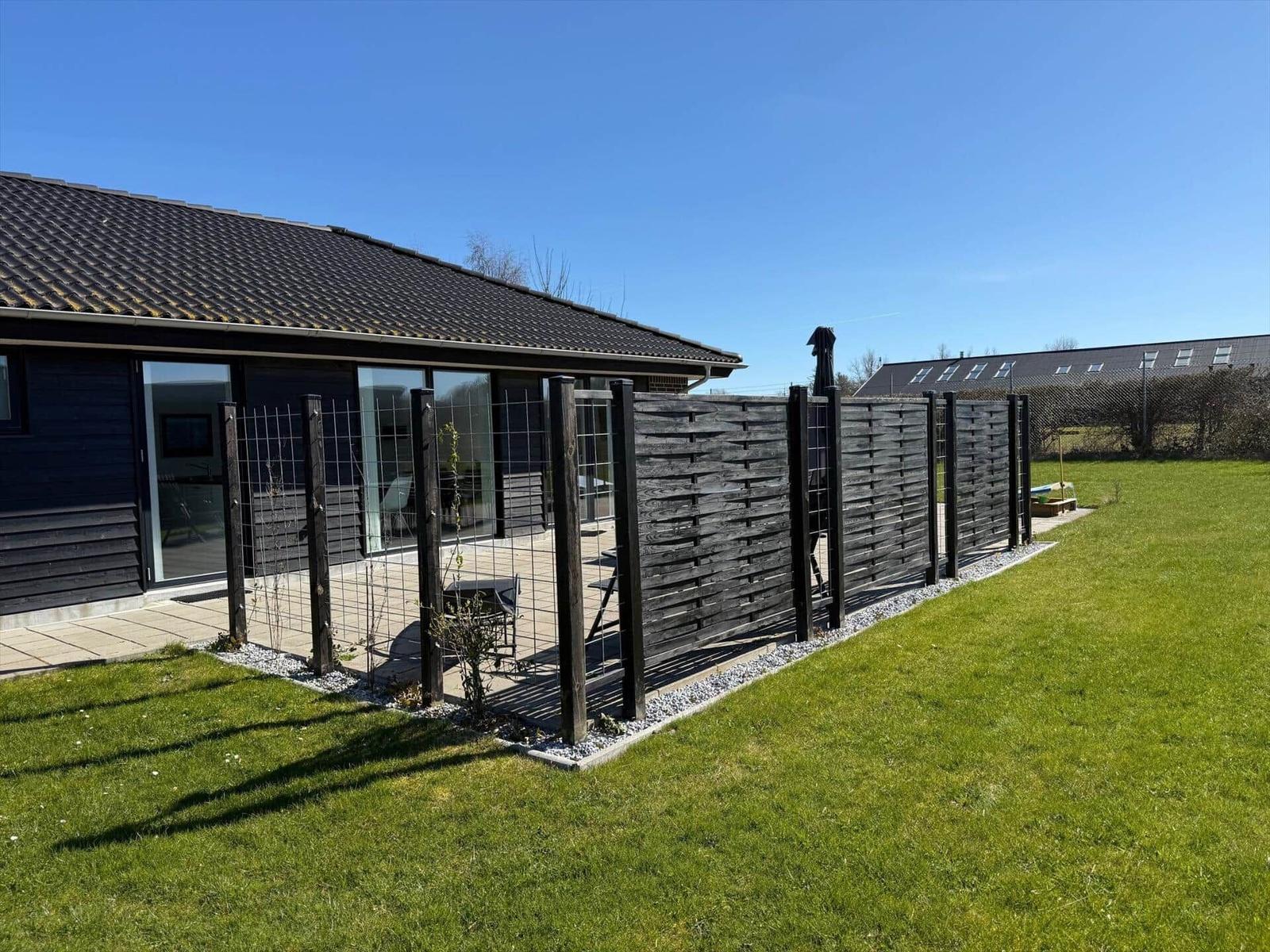 Hinterhof mit grünem Rasen, Holz-Zaun und Terrasse an modernem Haus.