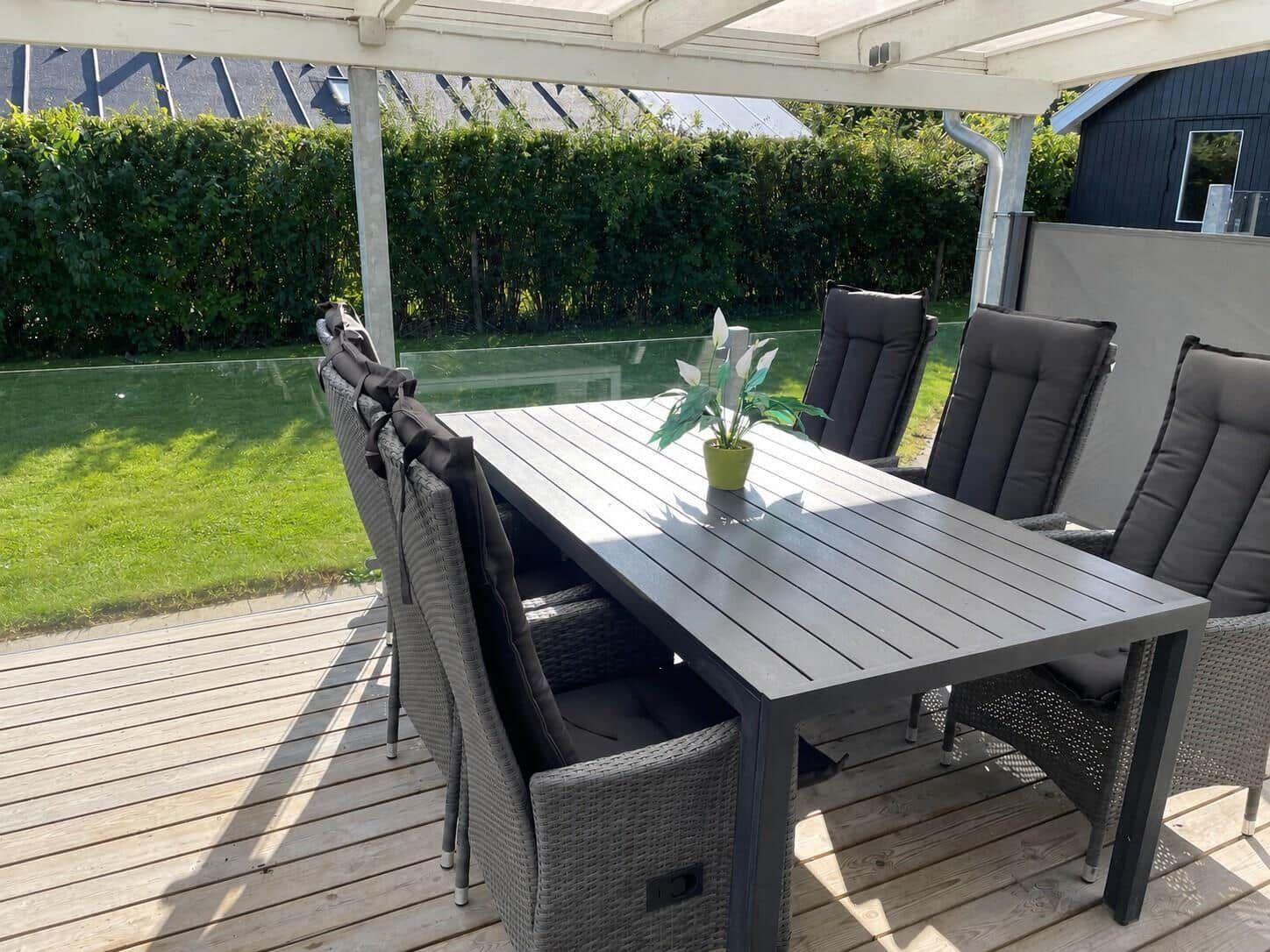 Terrasse mit Tisch und Stühlen unter einer Markise. Hintergrund: grüner Rasen und Hecke.