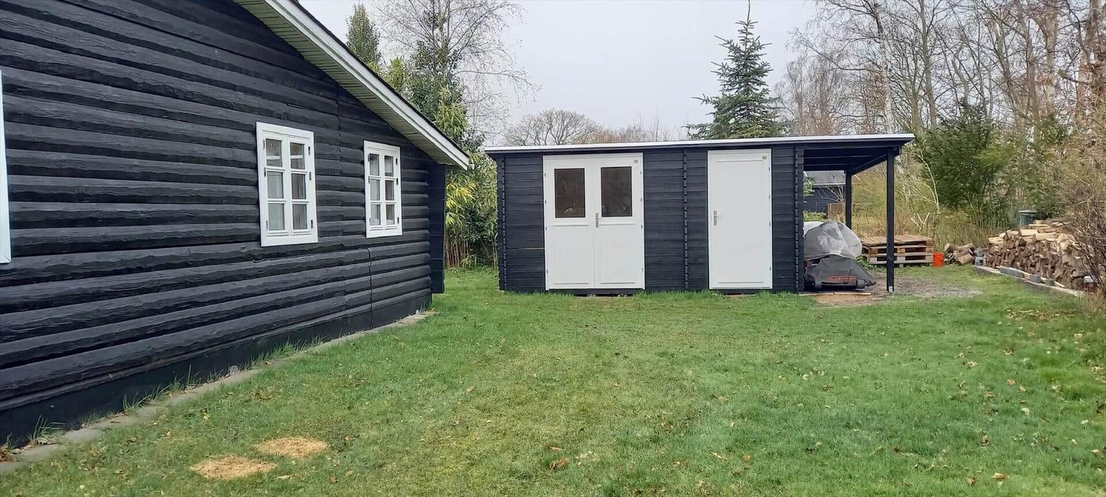 Schwarze Holzhütte mit weißen Türen und Fenstern im Garten.