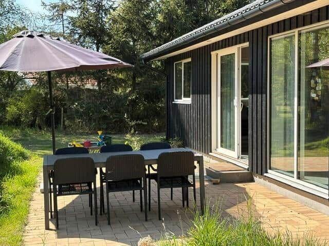 Terrace with table, chairs, and umbrella next to a house with glass front.