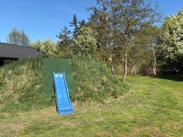 Blue slide in garden next to grass and trees.