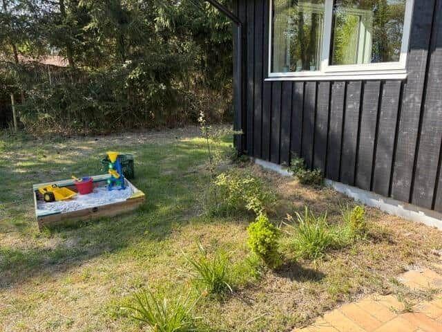 Backyard with sandbox and toys. Black siding and green area.