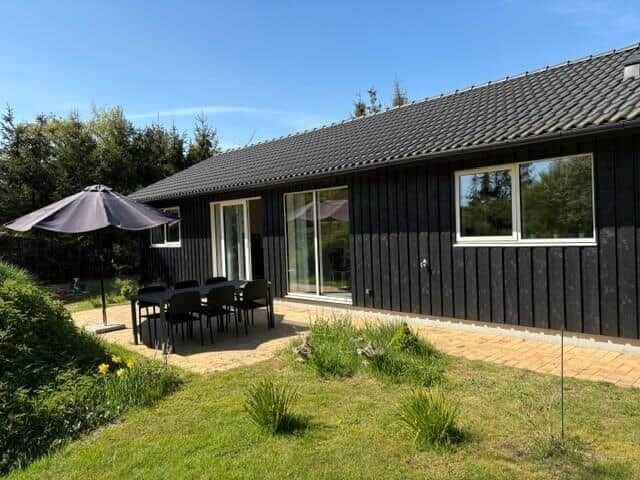 Black wooden house with terrace, seating group, and sunshade in the garden.