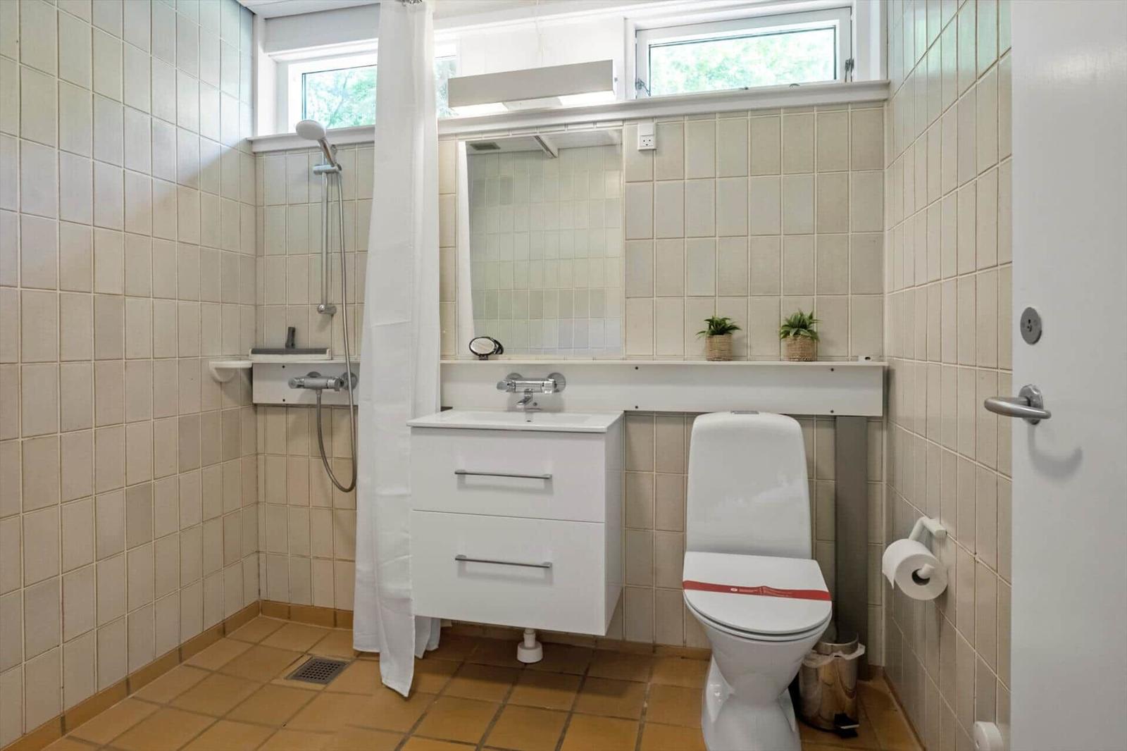 Badezimmer mit Dusche, Waschbecken und Toilette. Fliesenwand und Fenster.
