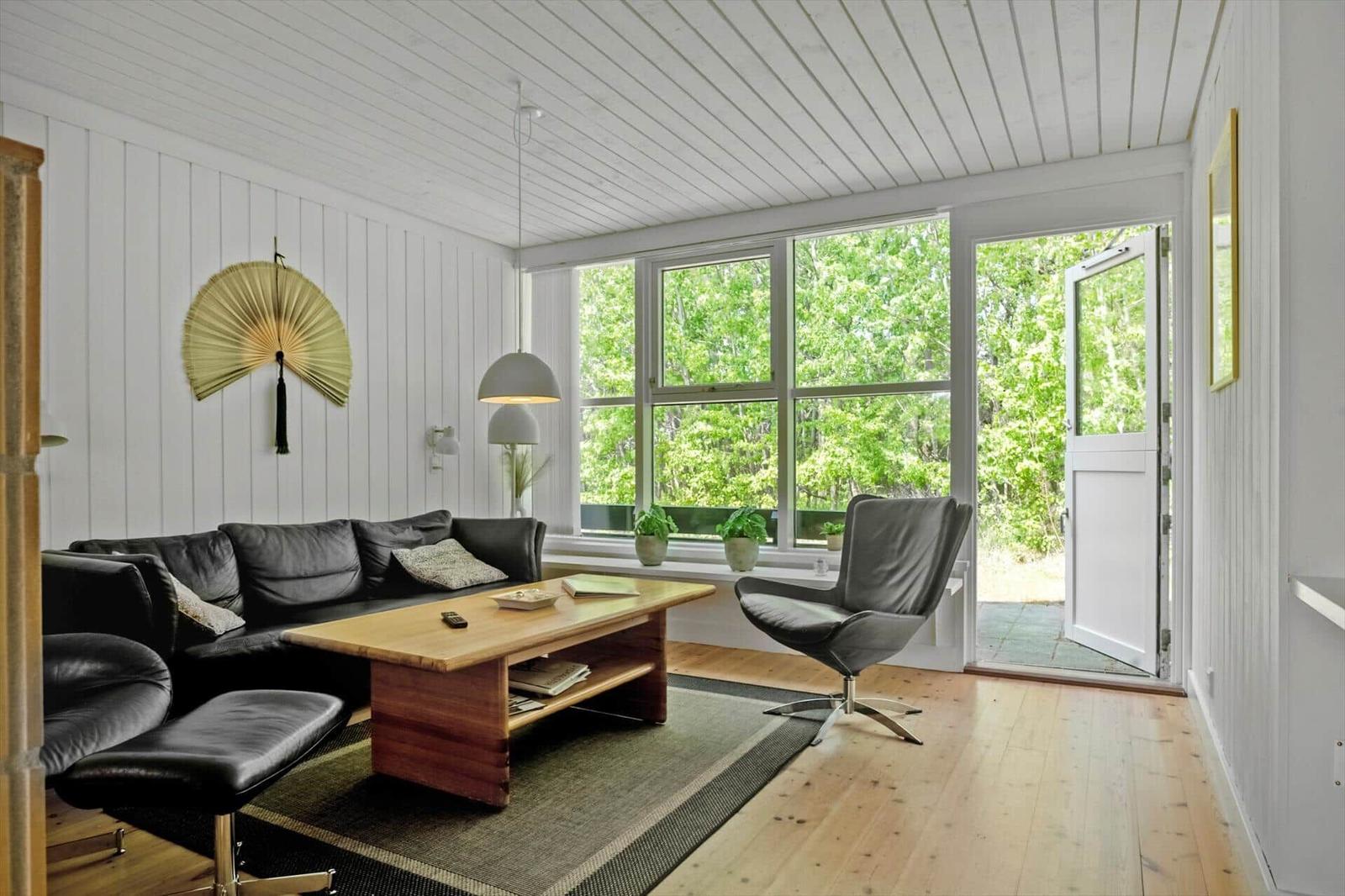 Ein Wohnzimmer mit schwarzer Couch, Holztisch und Sicht auf grüne Bäume.
