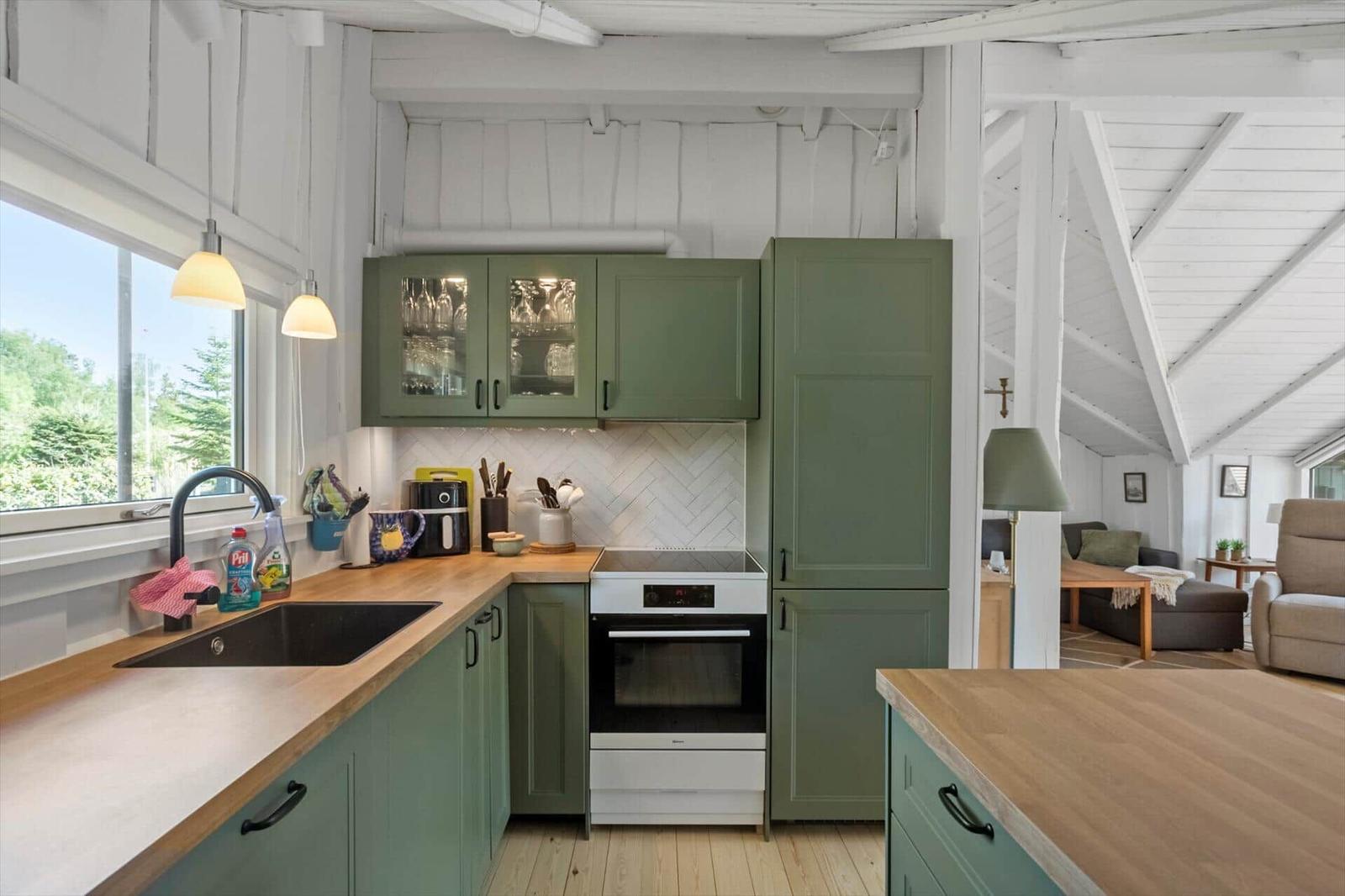 Kitchen with green cabinets, wooden surfaces, and view into living area.
