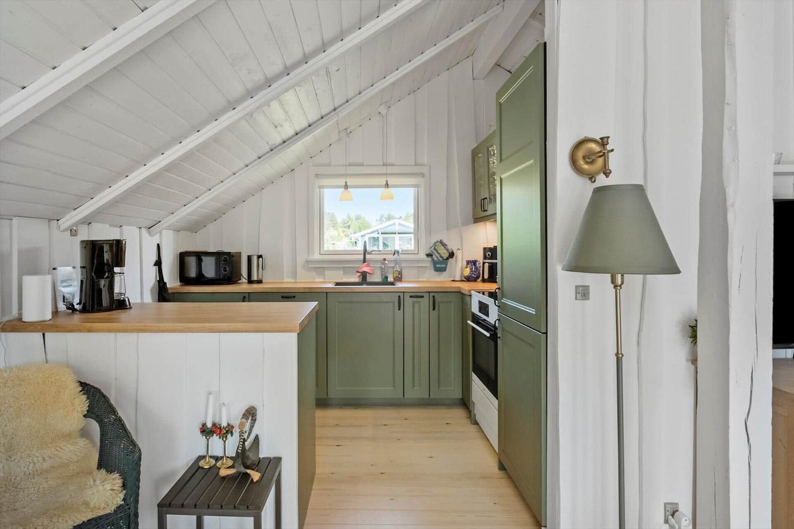 Kitchen with green cabinets, wooden floor, and sloped ceiling. Window, refrigerator, stove, and countertop visible.