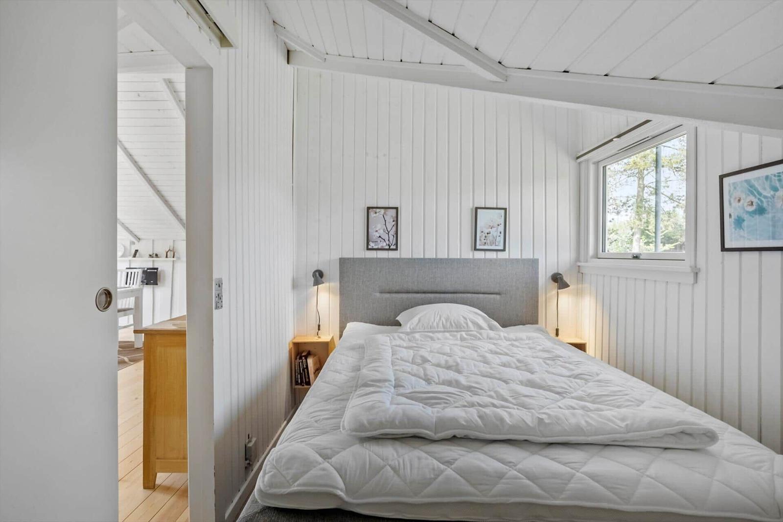 Bedroom with white wood walls, bed with white bedding, and window.