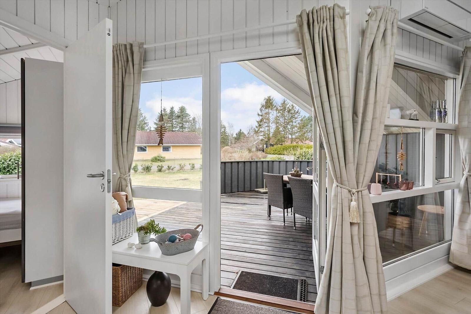 Durchgehende Glasfront öffnet sich auf eine Terrasse mit Tisch und Stühlen. Vor dem Haus liegt ein Garten.